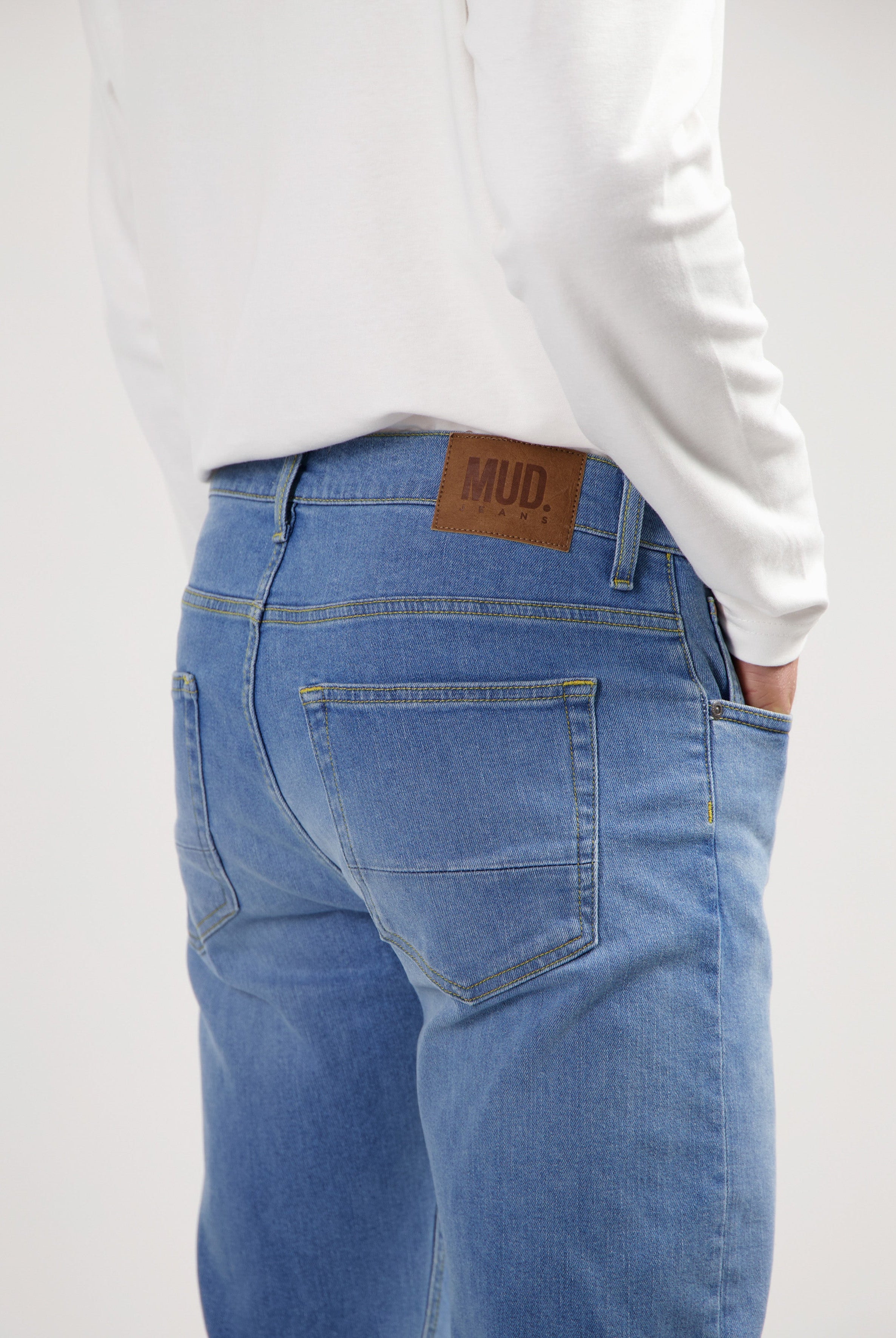 Sustainable MUD Jeans in light blue denim, crafted from organic cotton, paired with a casual gray shirt and white sneakers.