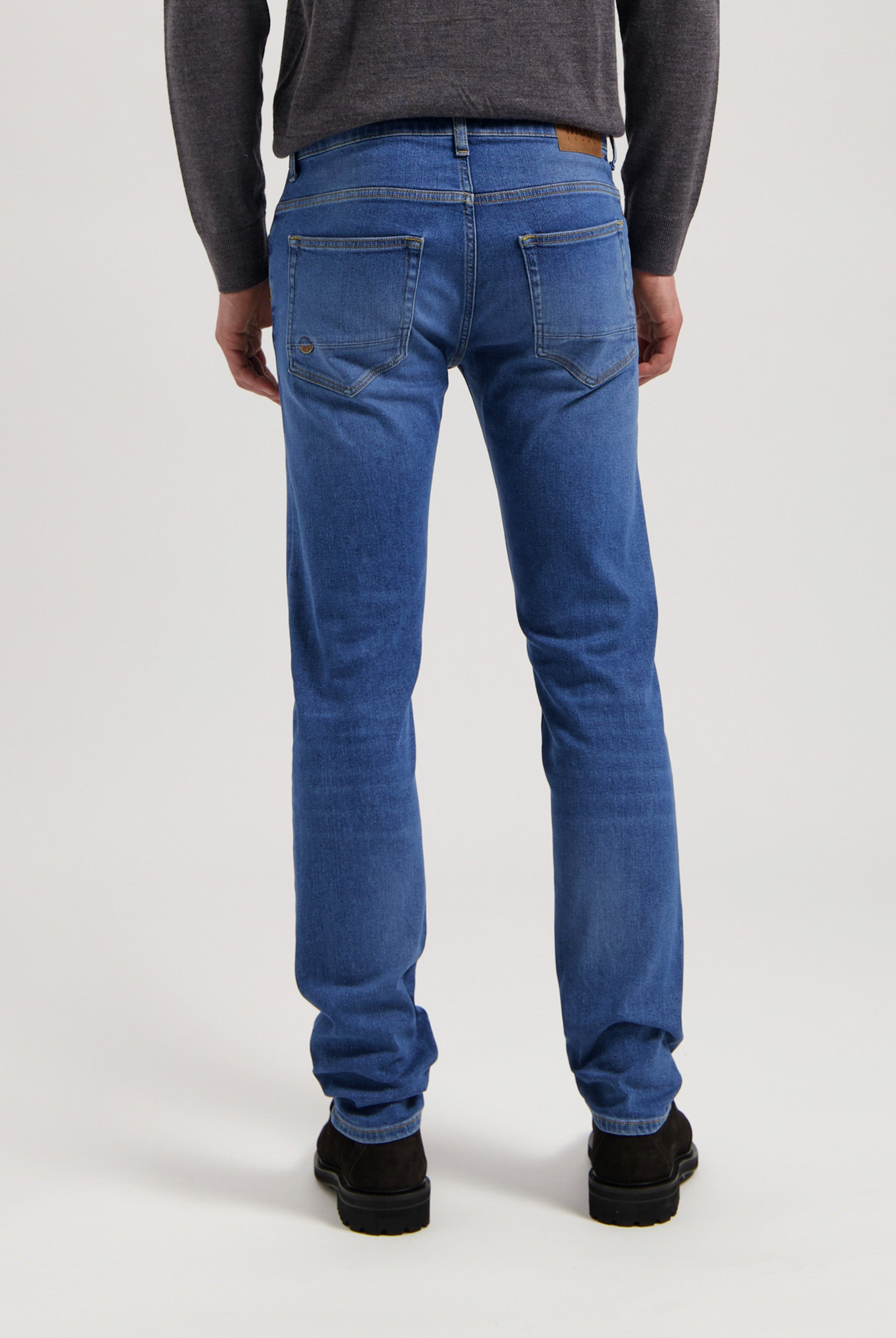 Sustainable MUD Jeans in deep indigo blue, crafted from eco-friendly materials, styled with a gray T-shirt and white sneakers.