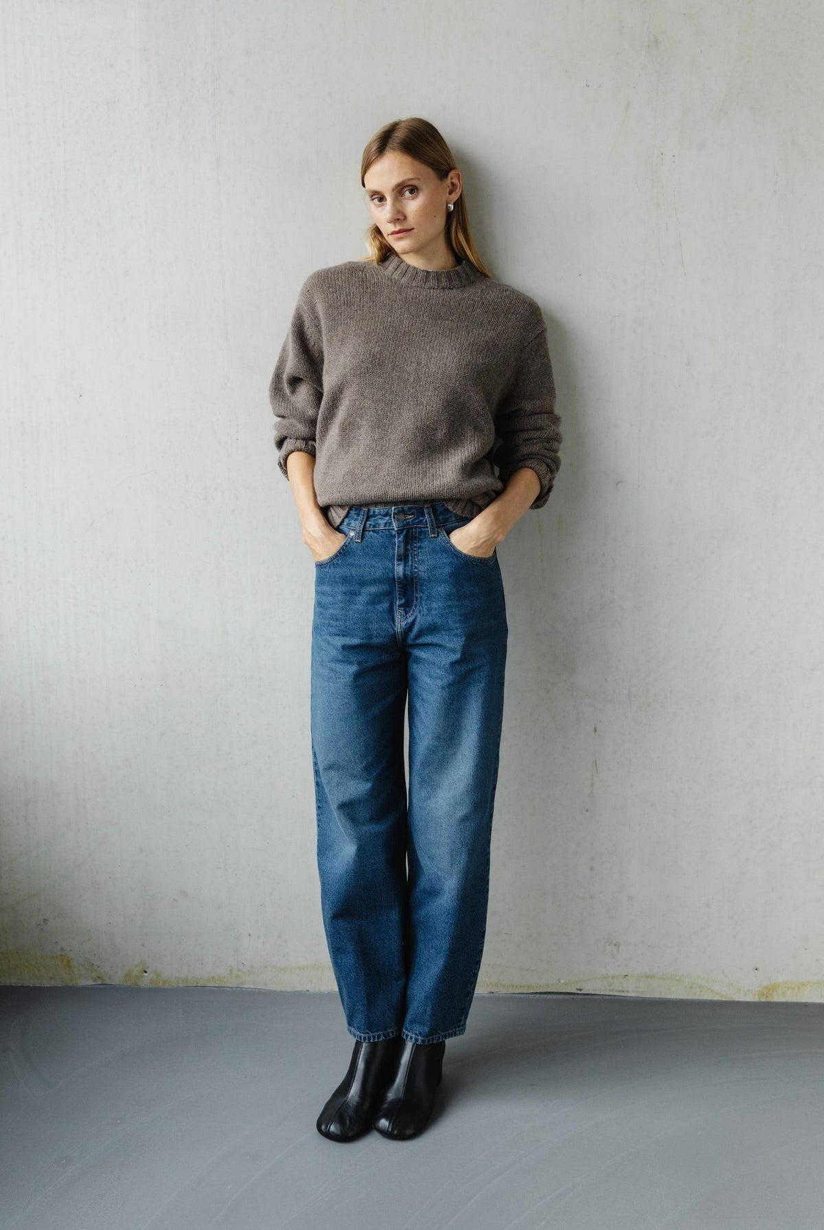 Casual fashion outfit featuring a gray knit sweater, high-waisted blue denim jeans, and black ankle boots against a plain background.