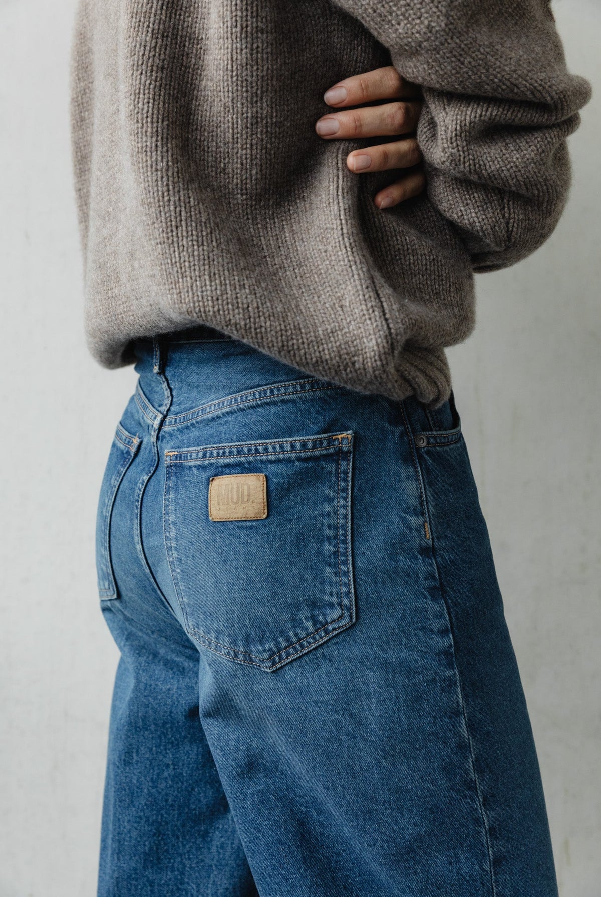 Person wearing blue MUD jeans paired with a cozy beige knitted sweater, showcasing a sustainable casual fashion look.