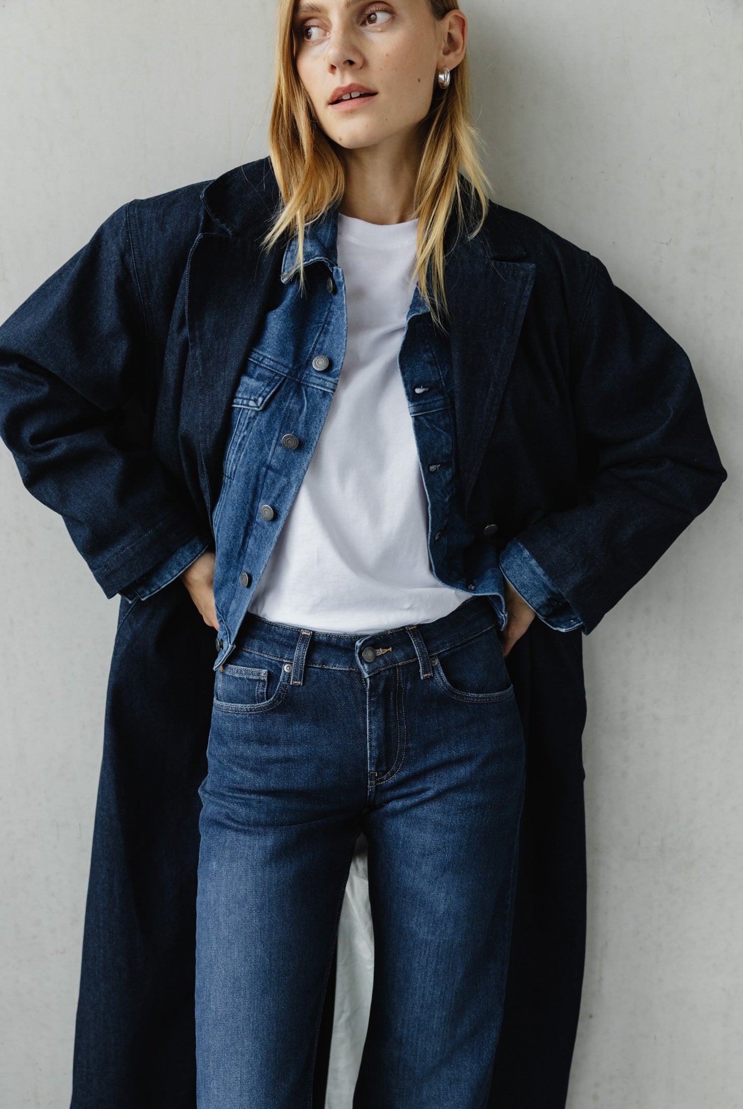 Model wearing layered blue denim jacket and jeans ensemble with a white T-shirt, styled with a long dark coat.