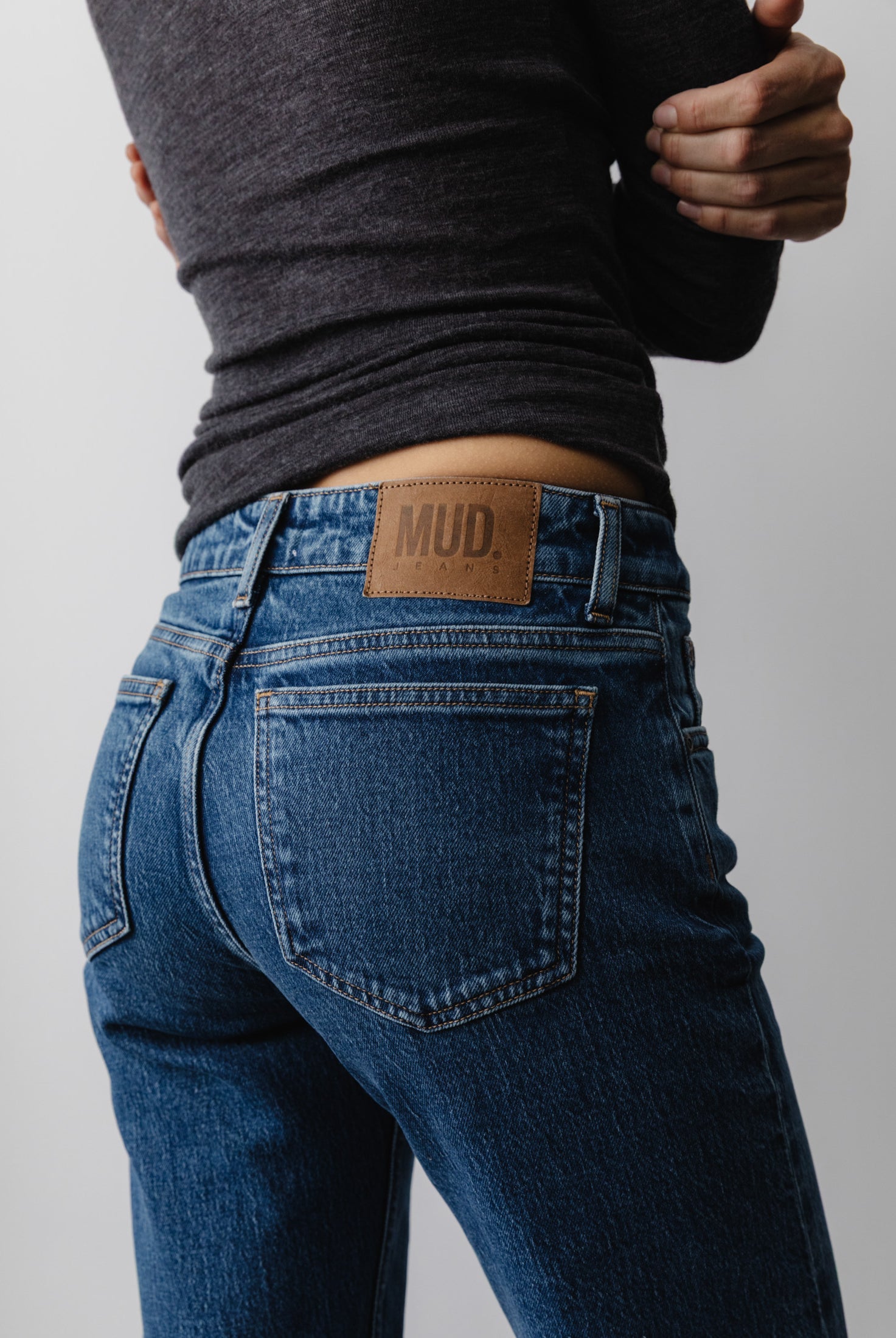 Dark blue MUD Jeans in organic cotton, showcasing high-waisted, slim-fit design with a gray long-sleeve top.