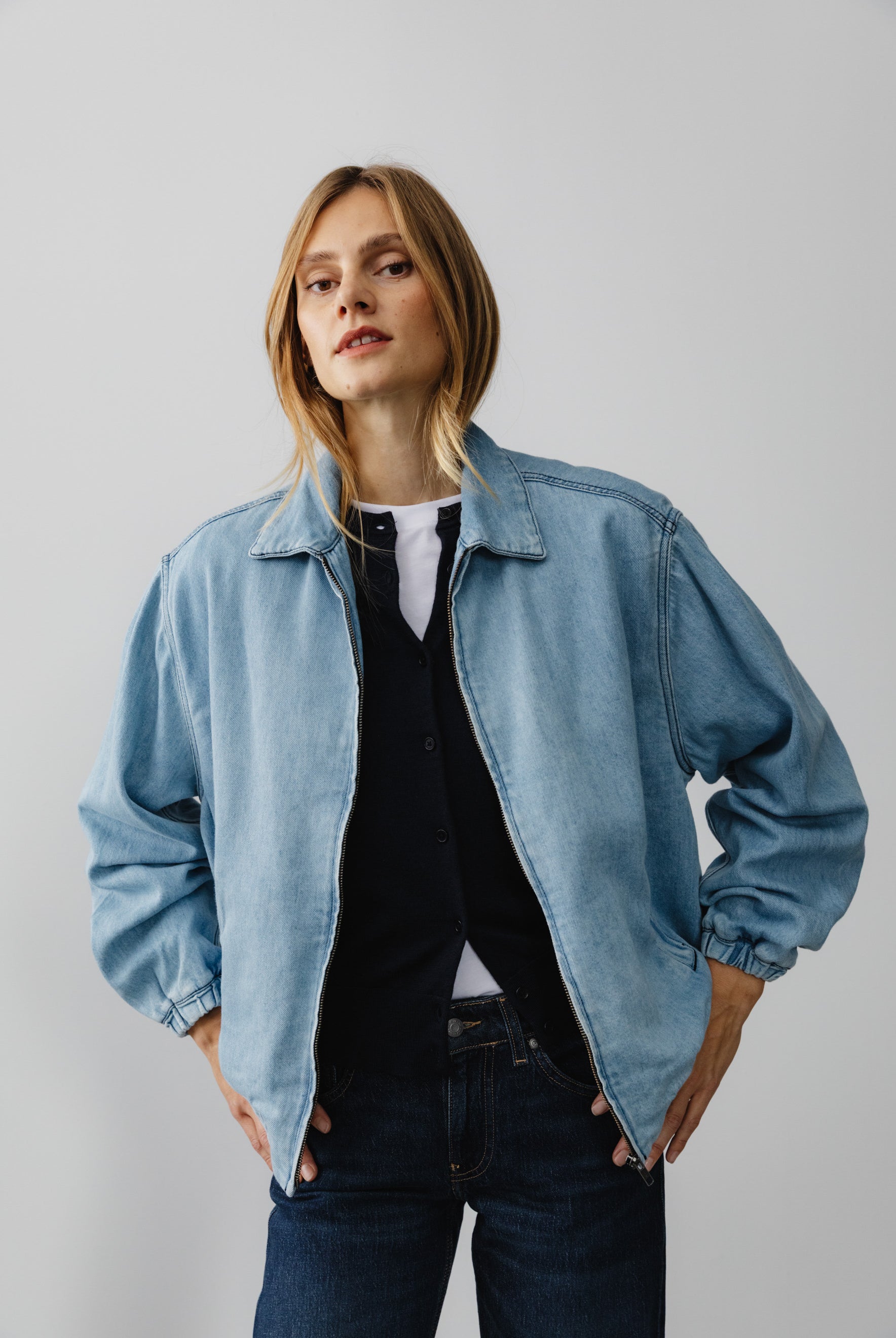 A casual light blue denim jacket worn over a navy shirt and white top, paired with dark blue jeans, perfect for a relaxed style.