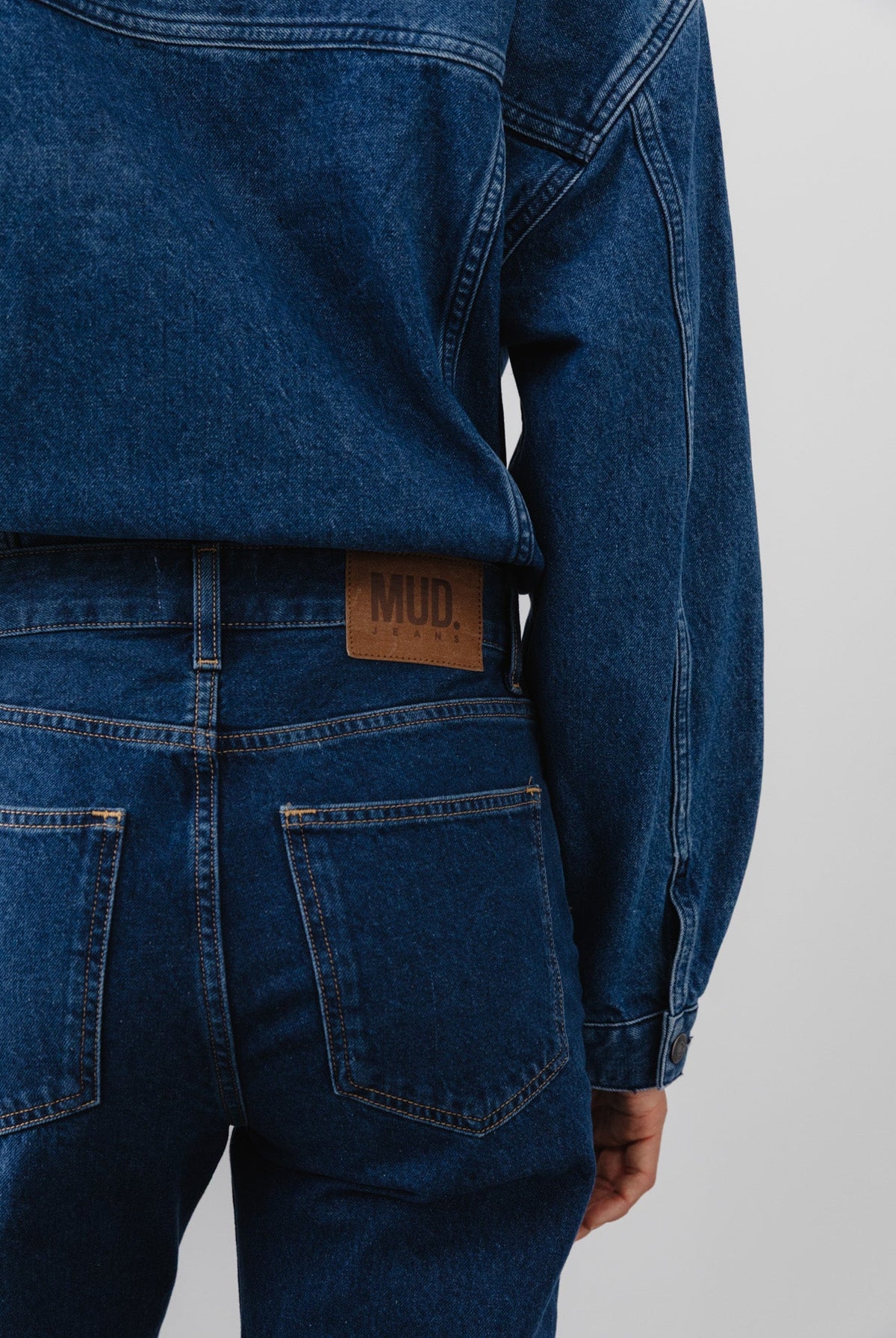 Back view of recycled dark blue denim jacket and jeans set, featuring MUD Jeans logo on leather patch above pocket.