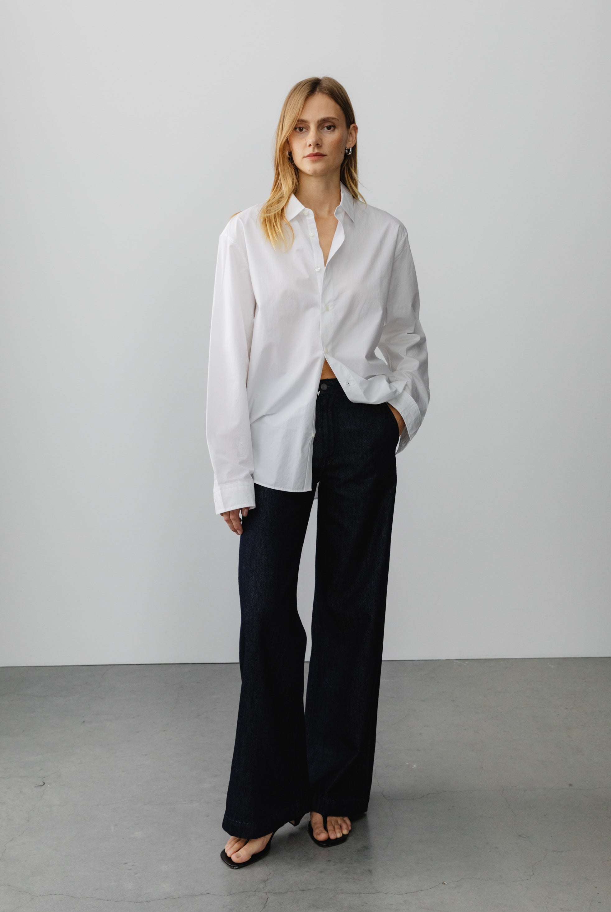 Oversized white cotton button-up shirt paired with black wide-leg pants on gray concrete floor background.