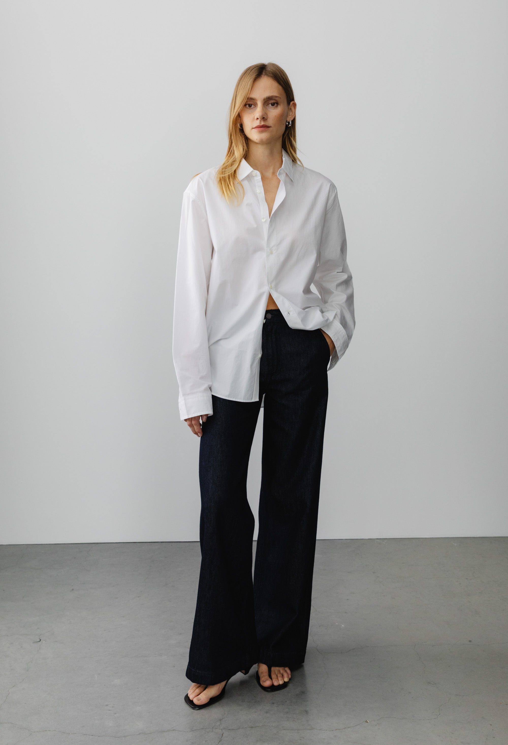 Oversized white cotton button-up shirt paired with black wide-leg pants on gray concrete floor background.