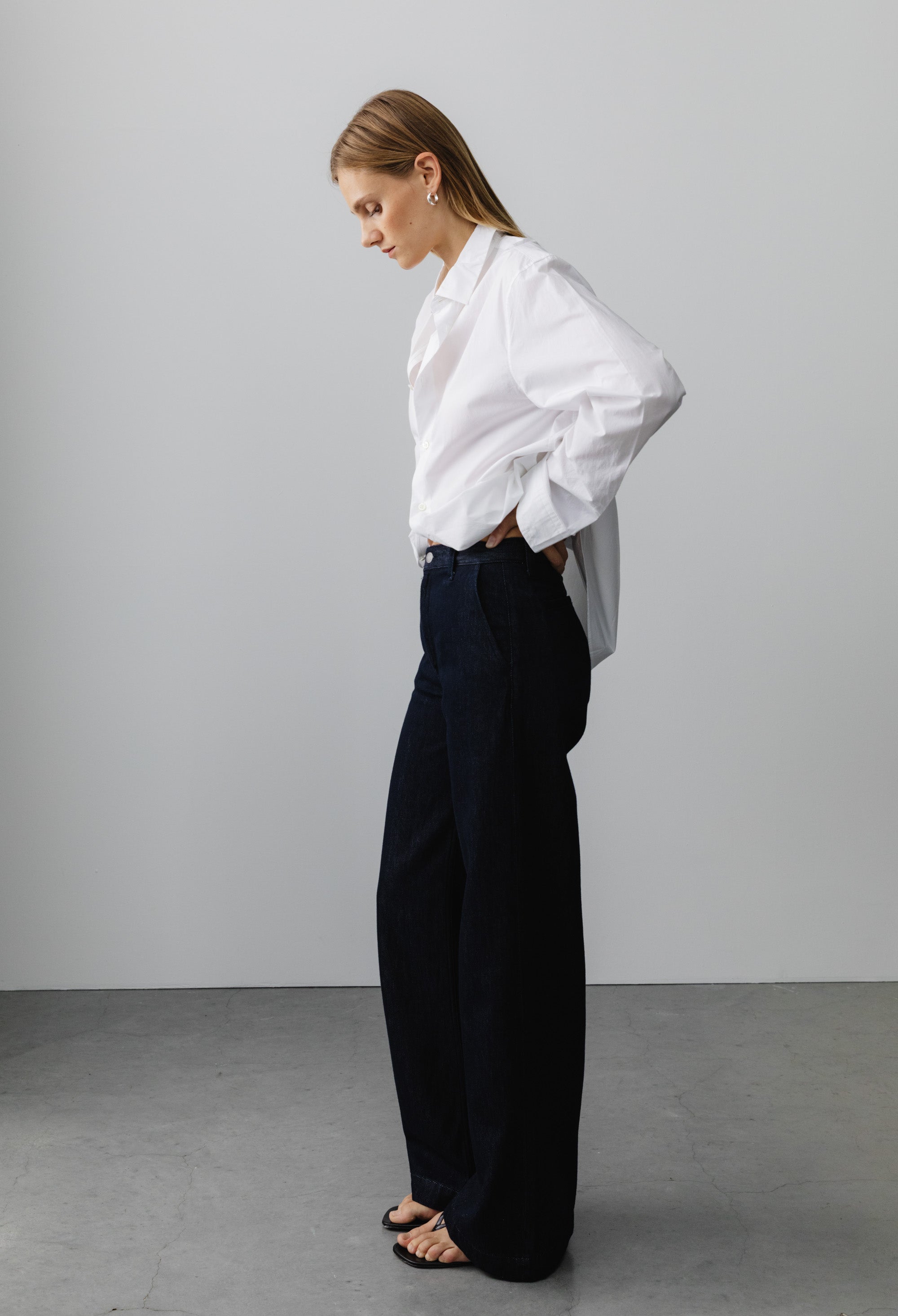 A model wearing a crisp white button-up shirt paired with wide-leg dark blue denim jeans and black sandals.