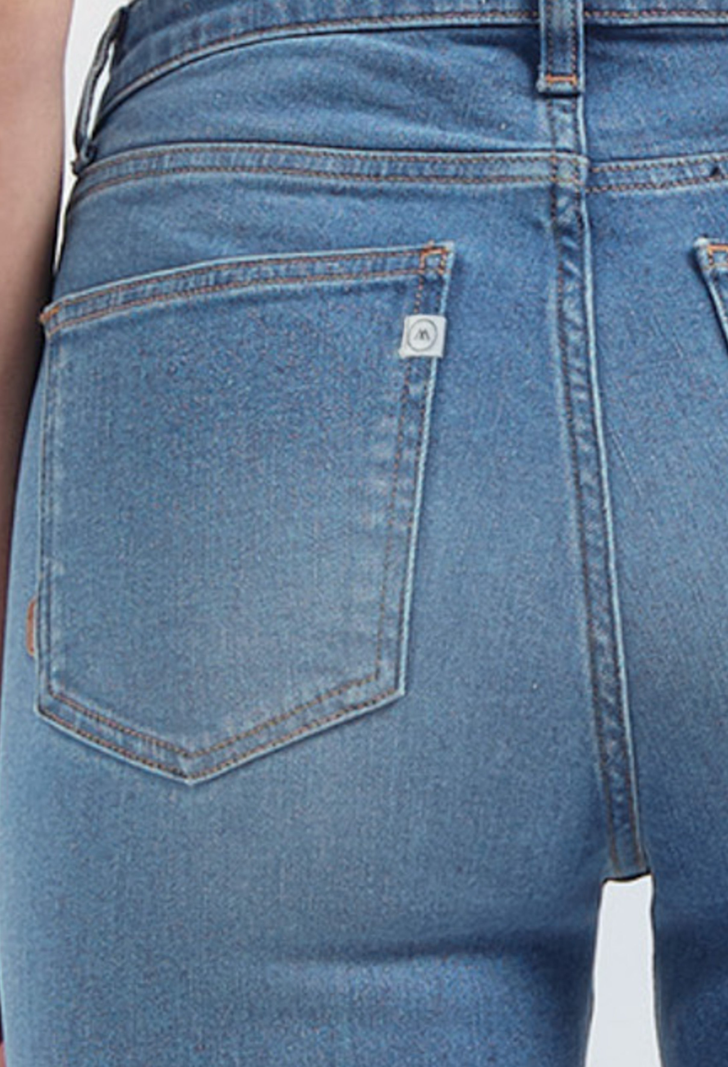 Close-up of light blue denim jeans with visible back pocket stitching and a subtle logo tag near the waistband.