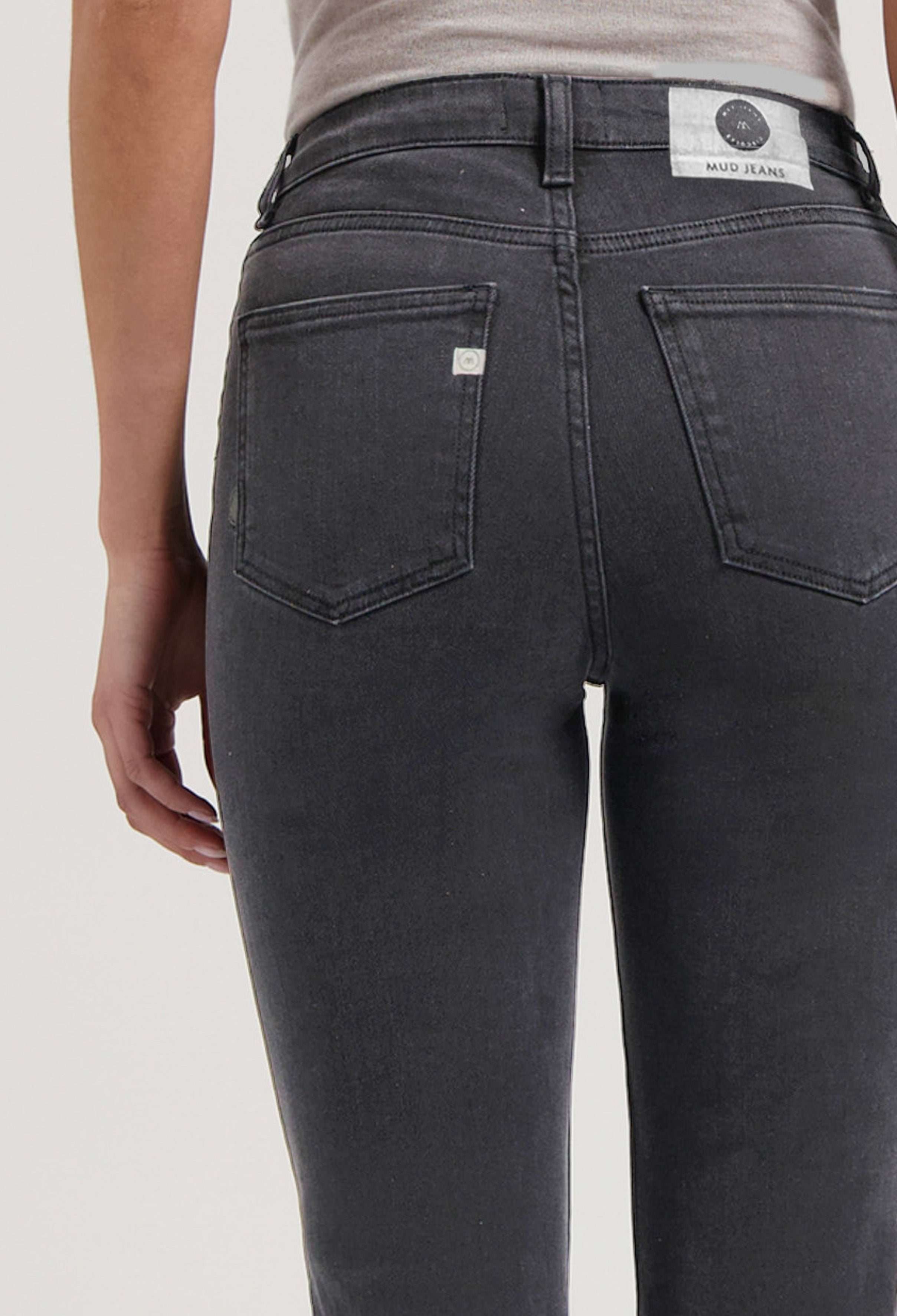 Close-up of dark gray MUD Jeans denim showcasing back pockets and sustainable fabric detail, worn with a light beige top.