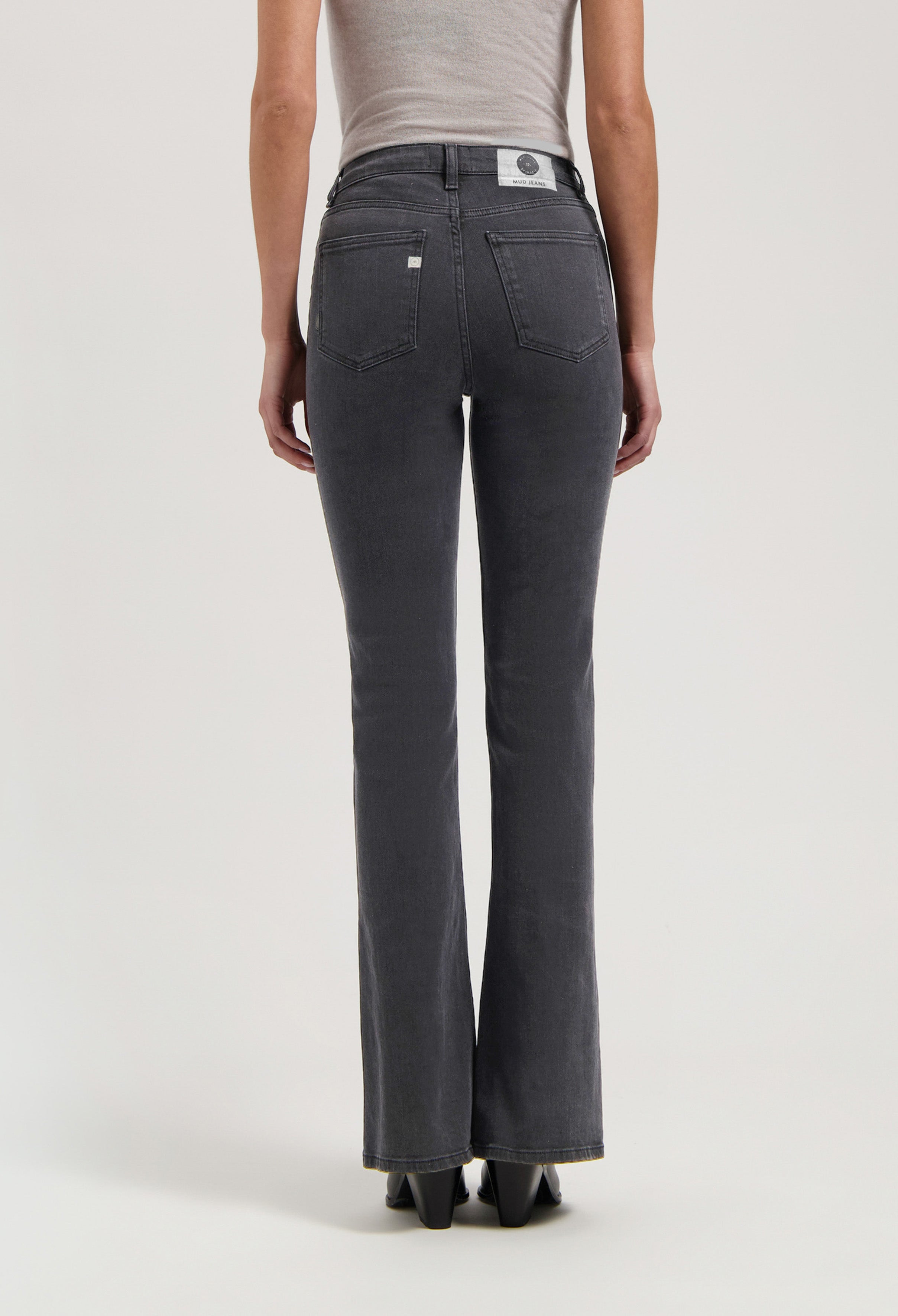 Back view of sustainable MUD Jeans in washed black, showcasing straight-leg fit, paired with a fitted beige top for modern style.