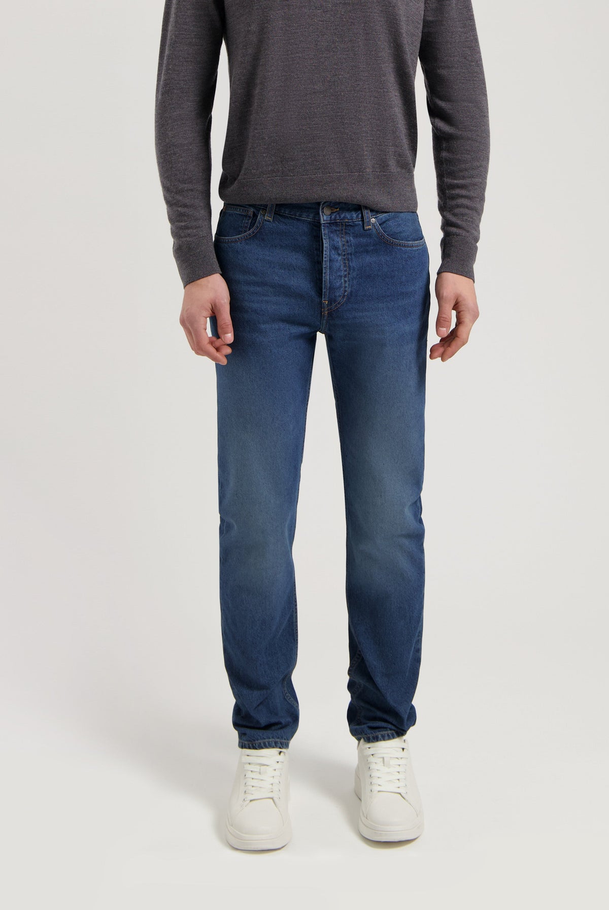 Sustainable MUD Jeans in classic blue denim with a slim fit, crafted ethically, paired with a gray sweater and white sneakers.