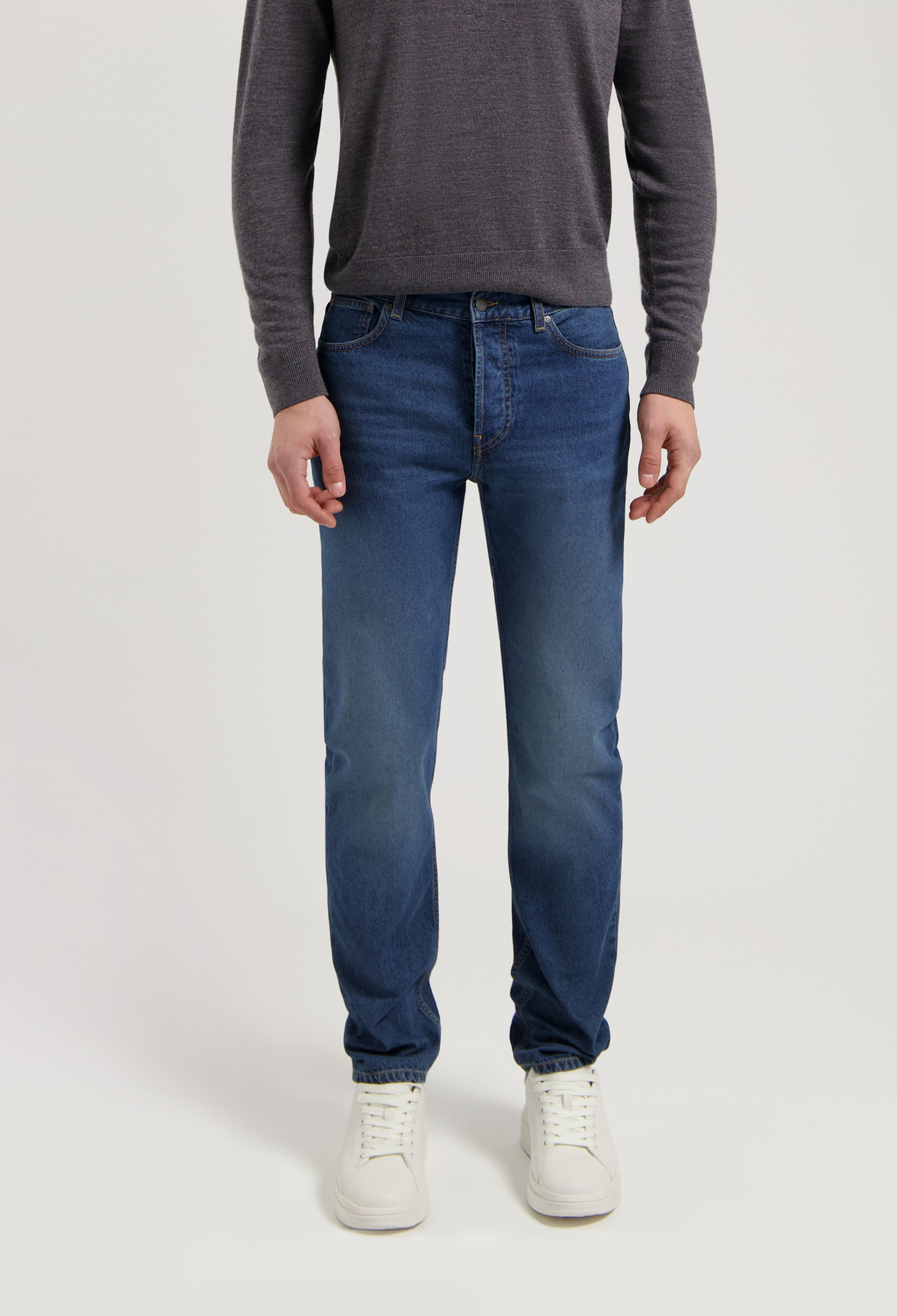 Sustainable MUD Jeans in classic blue denim with a slim fit, crafted ethically, paired with a gray sweater and white sneakers.