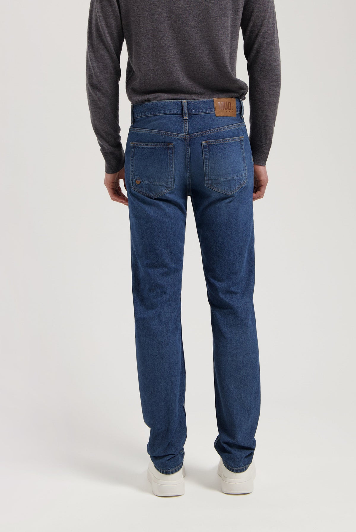 Sustainable MUD Jeans in deep blue denim, crafted ethically from organic cotton, shown with a dark gray sweater.
