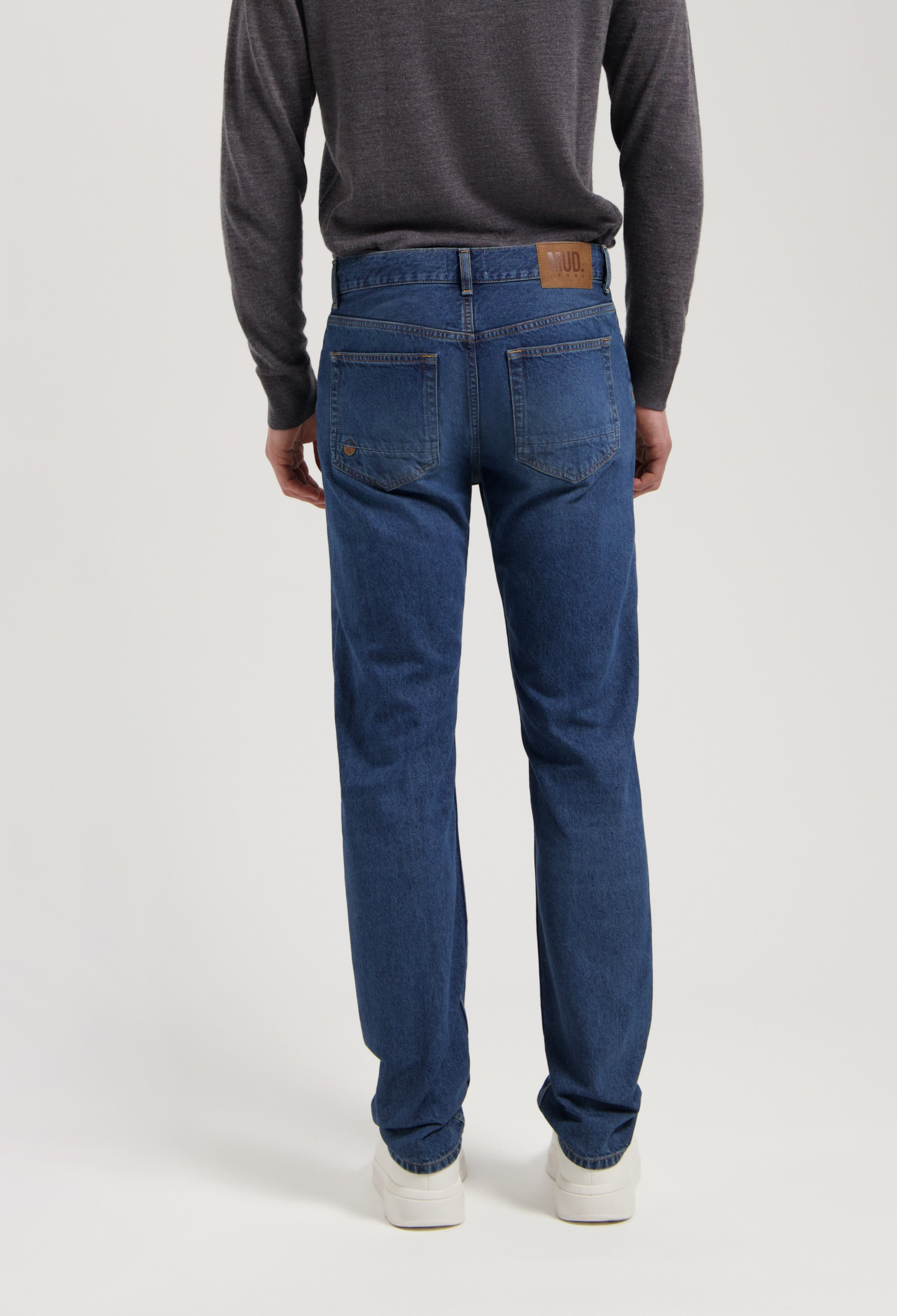 Sustainable MUD Jeans in deep blue denim, crafted ethically from organic cotton, shown with a dark gray sweater.