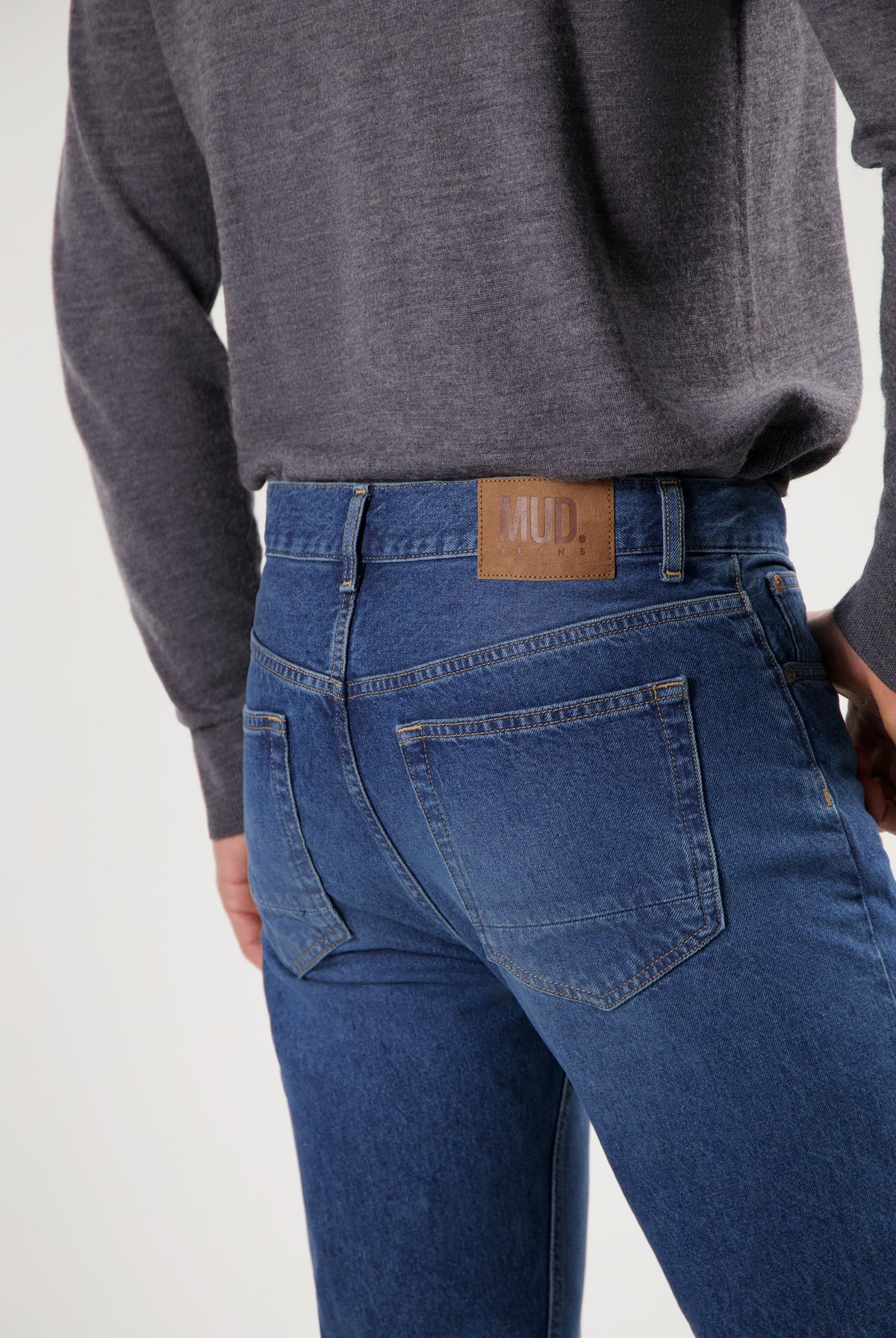 Sustainable MUD Jeans featuring classic blue denim crafted ethically, worn with a soft charcoal gray sweater.