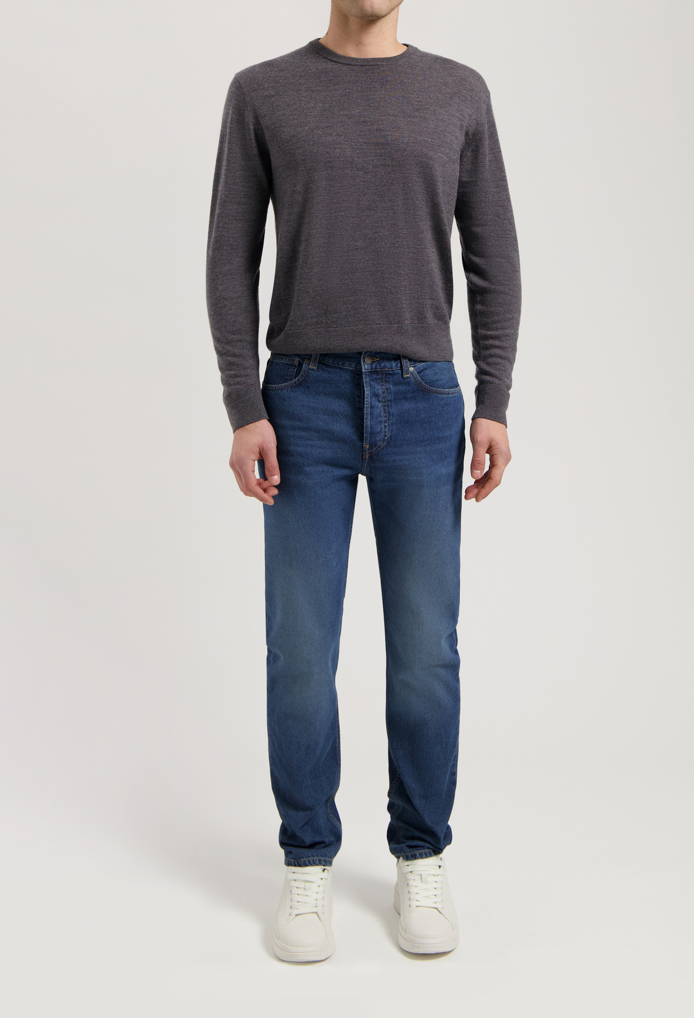 Sustainable MUD Jeans crafted from organic cotton, in a classic blue denim, paired with a gray sweater and white sneakers.