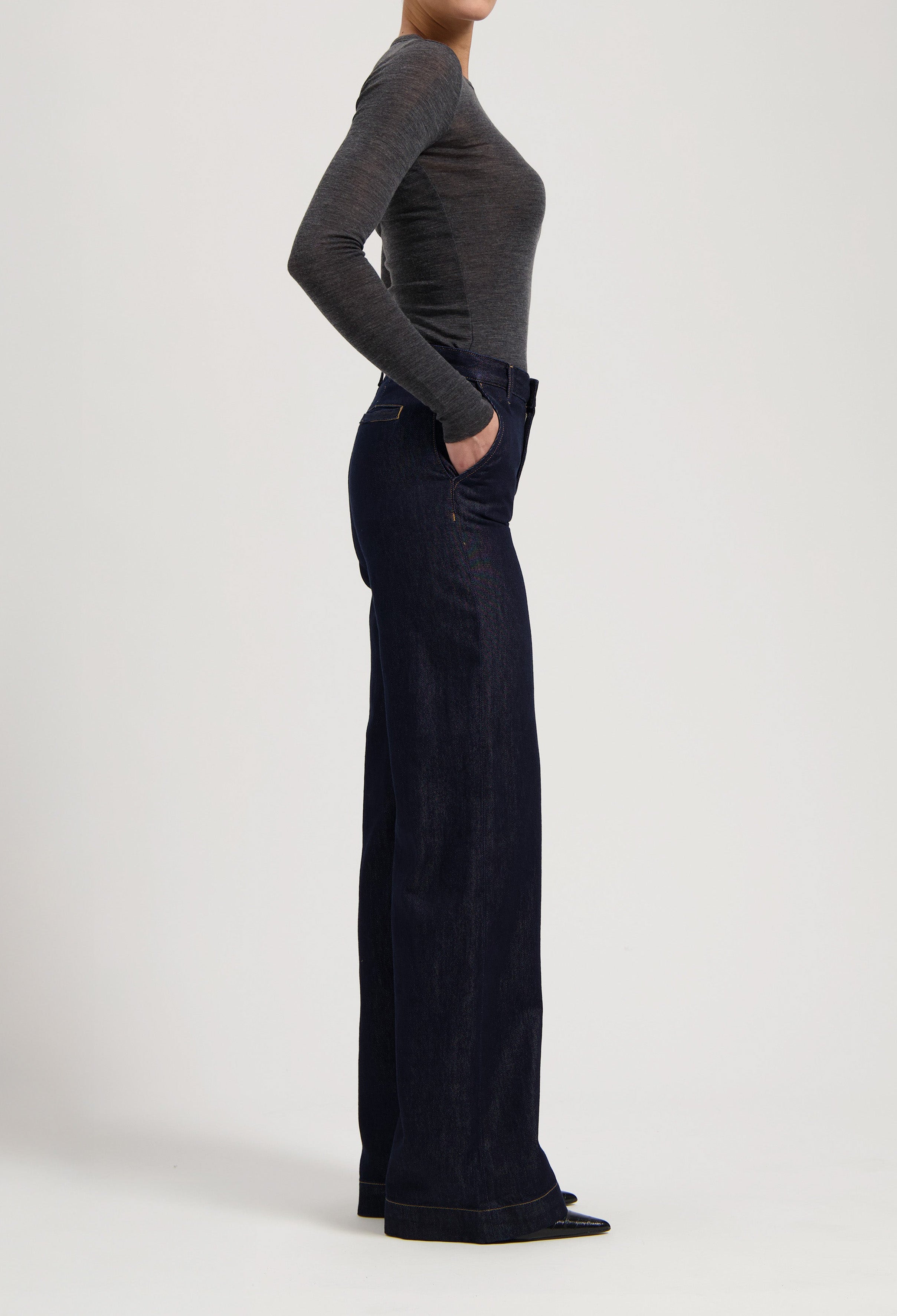 Model wearing dark blue, high-waisted denim jeans paired with a fitted gray long-sleeve shirt, showcasing a side profile.