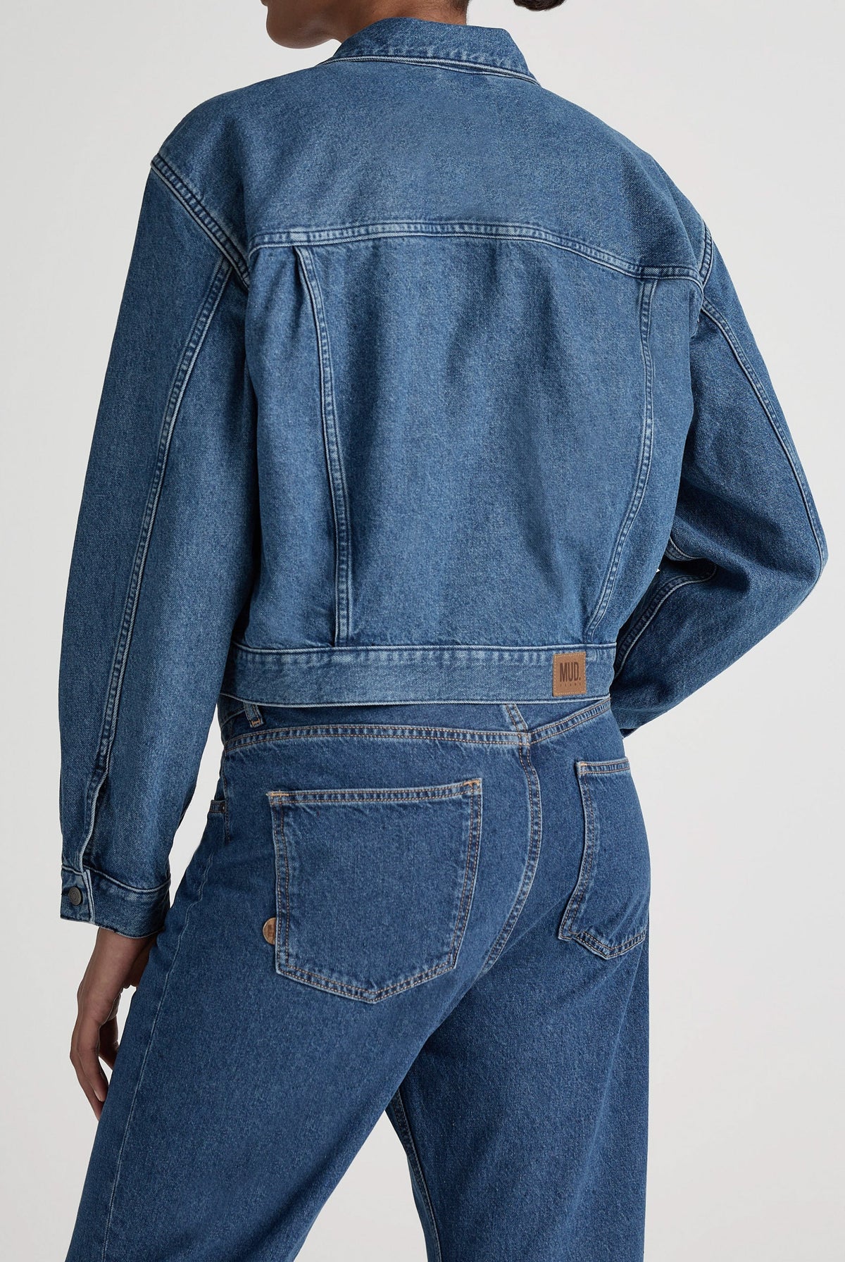 A stylish blue denim jacket paired with matching high-waisted jeans, showcasing sustainable fashion by MUD Jeans.