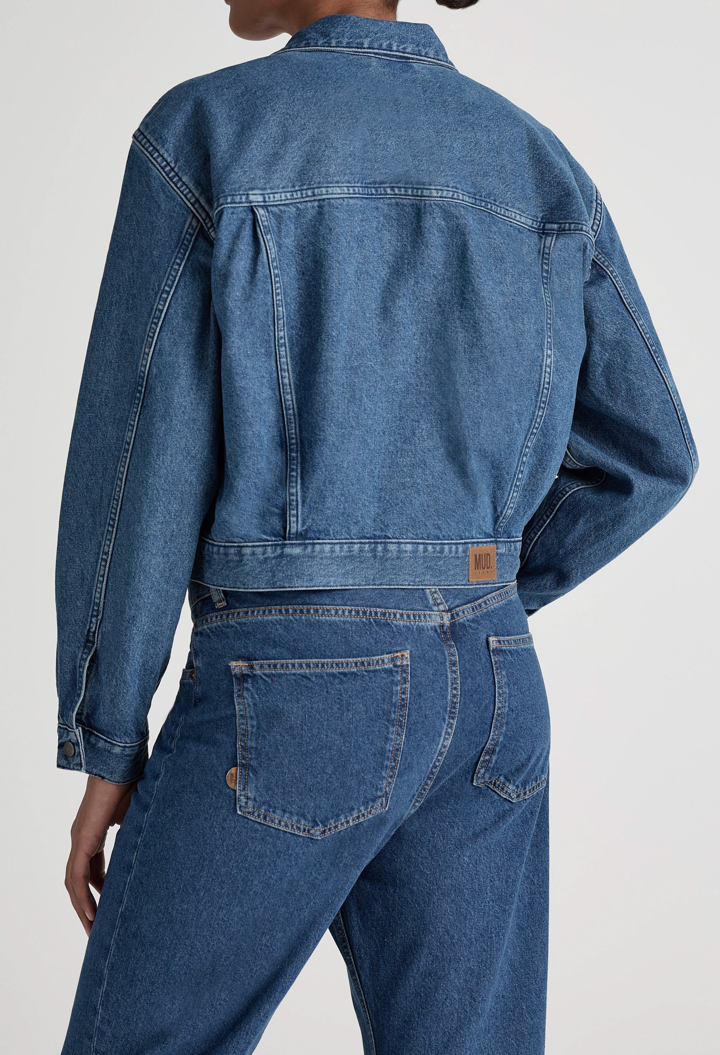 A stylish blue denim jacket paired with matching high-waisted jeans, showcasing sustainable fashion by MUD Jeans.