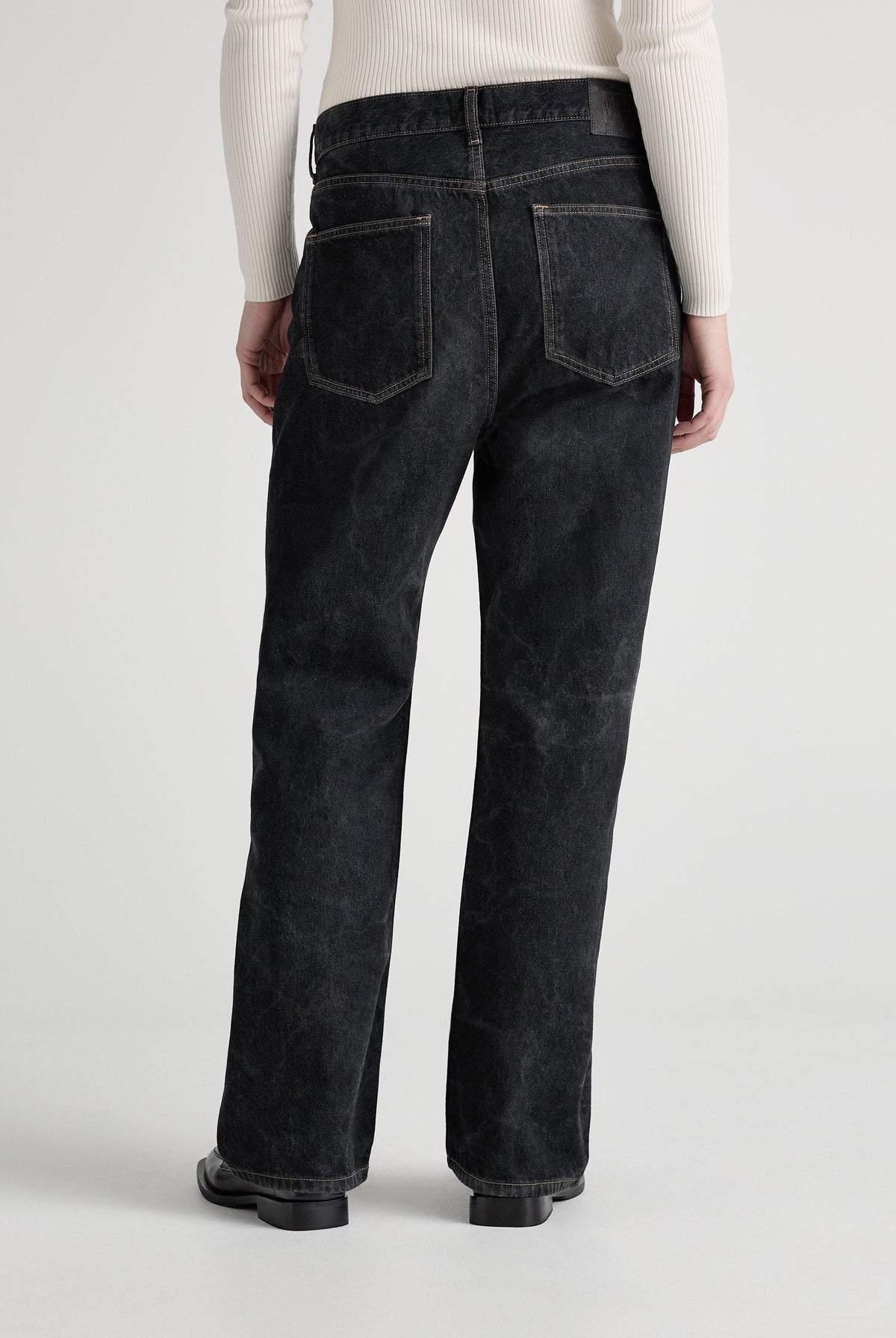Wide-leg black denim jeans with back pockets, shown from the rear, paired with a cream ribbed long-sleeve top.