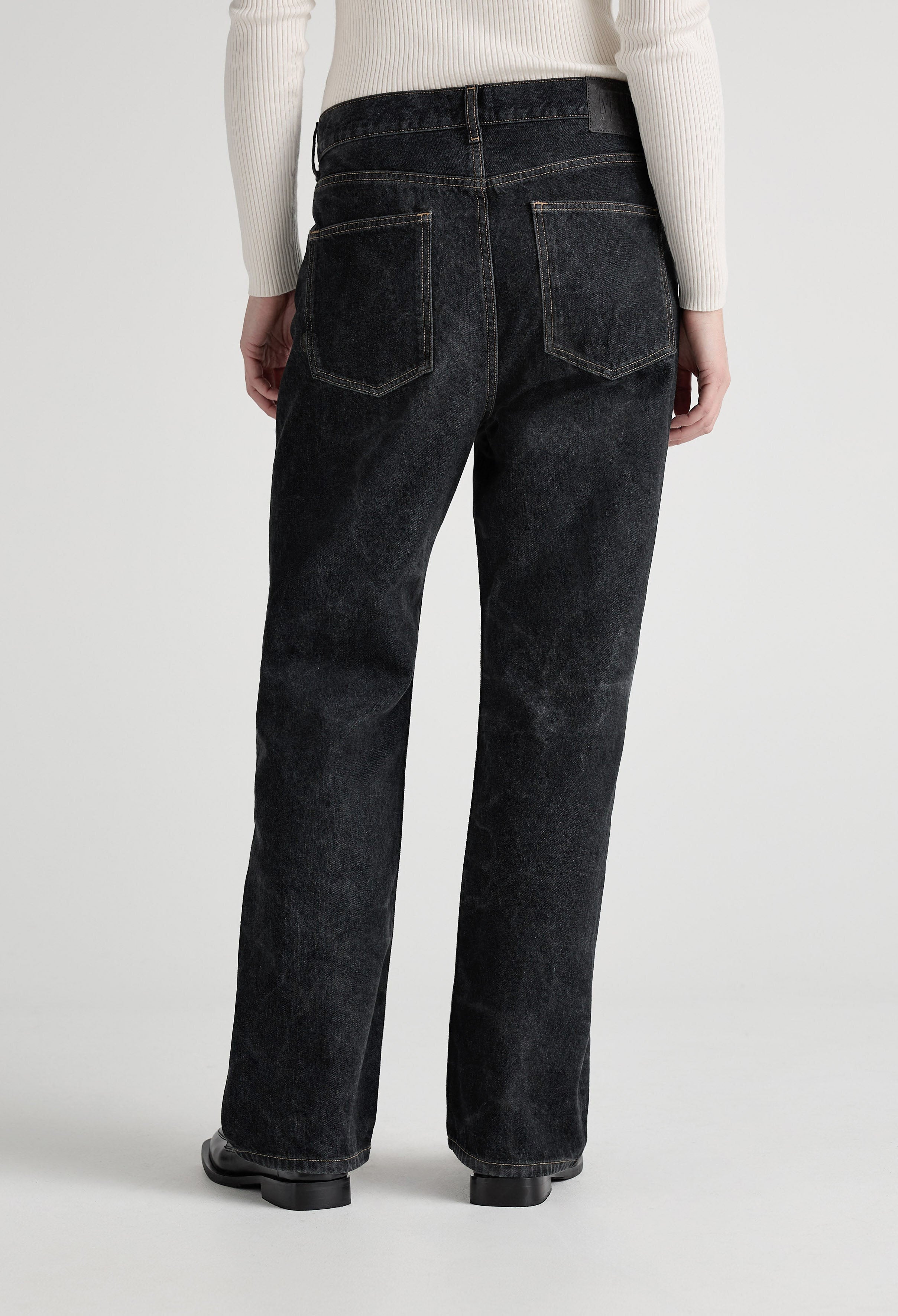 Wide-leg black denim jeans with back pockets, shown from the rear, paired with a cream ribbed long-sleeve top.