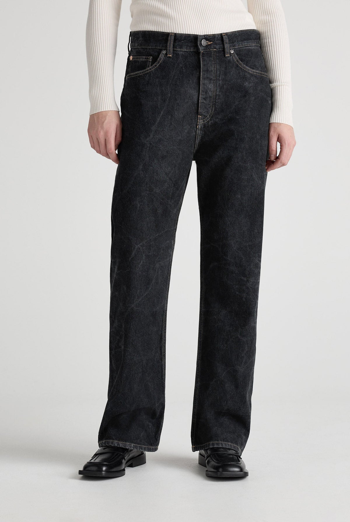 A model wearing loose-fitting black denim jeans with a ribbed, white long-sleeve top and black leather shoes.