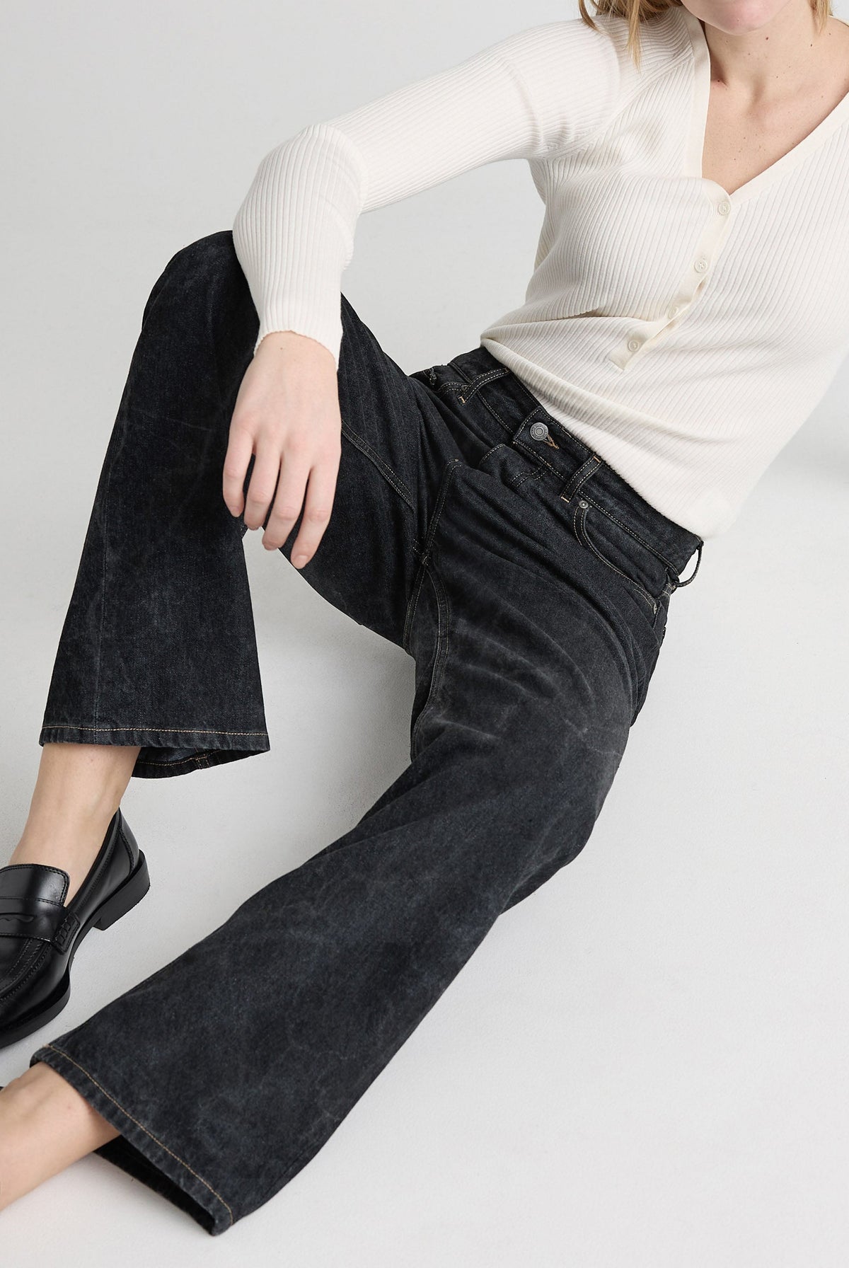 Casual black jeans paired with a ribbed white sweater, featuring wide-leg cut and button details, worn with black loafers.