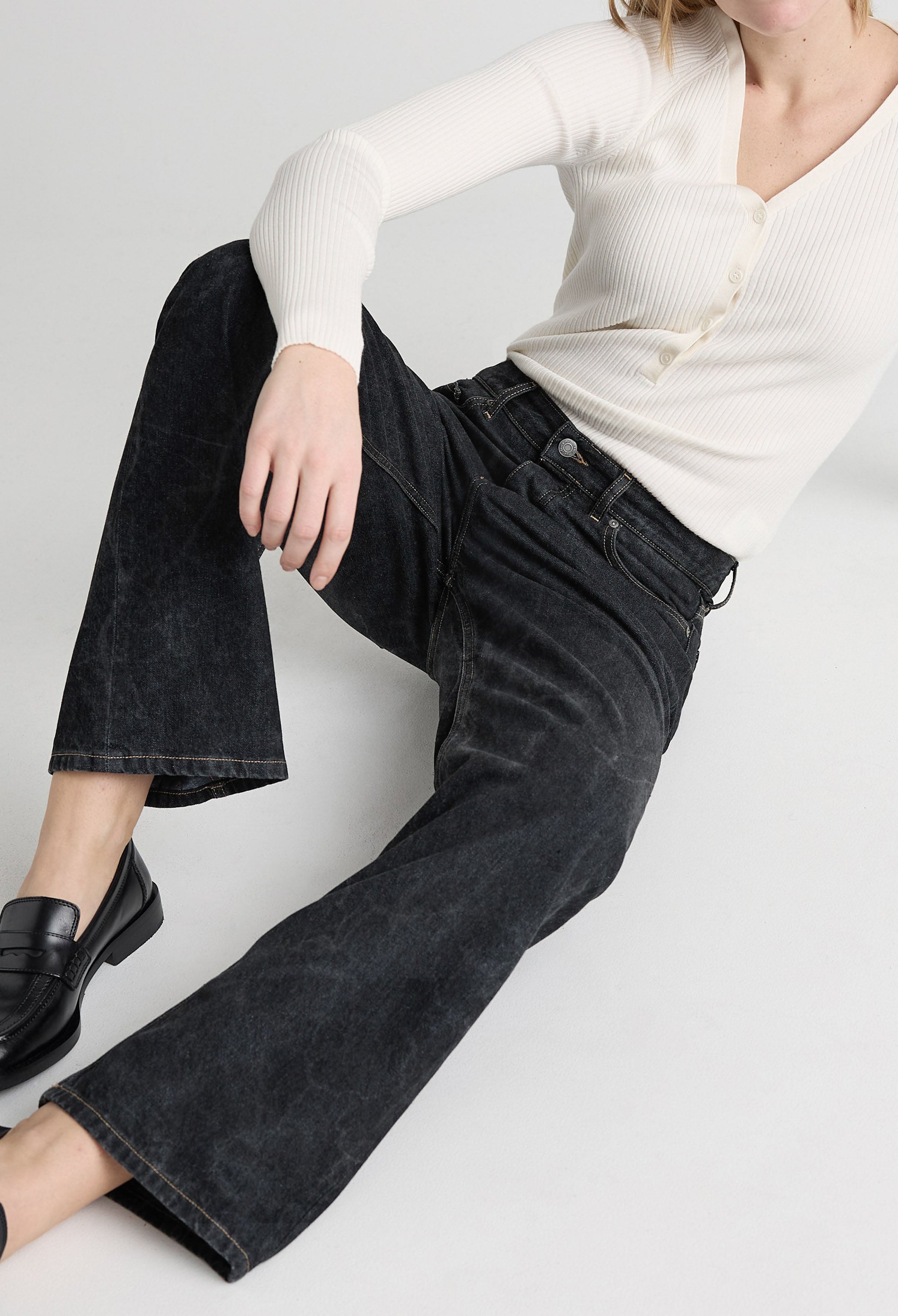 Casual black jeans paired with a ribbed white sweater, featuring wide-leg cut and button details, worn with black loafers.