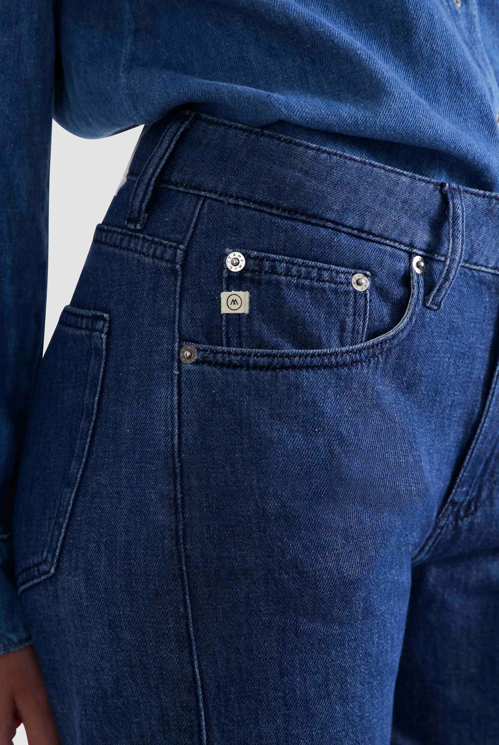 Dark blue denim jeans with silver button accents, featuring a close-up on the pocket and stitching details.