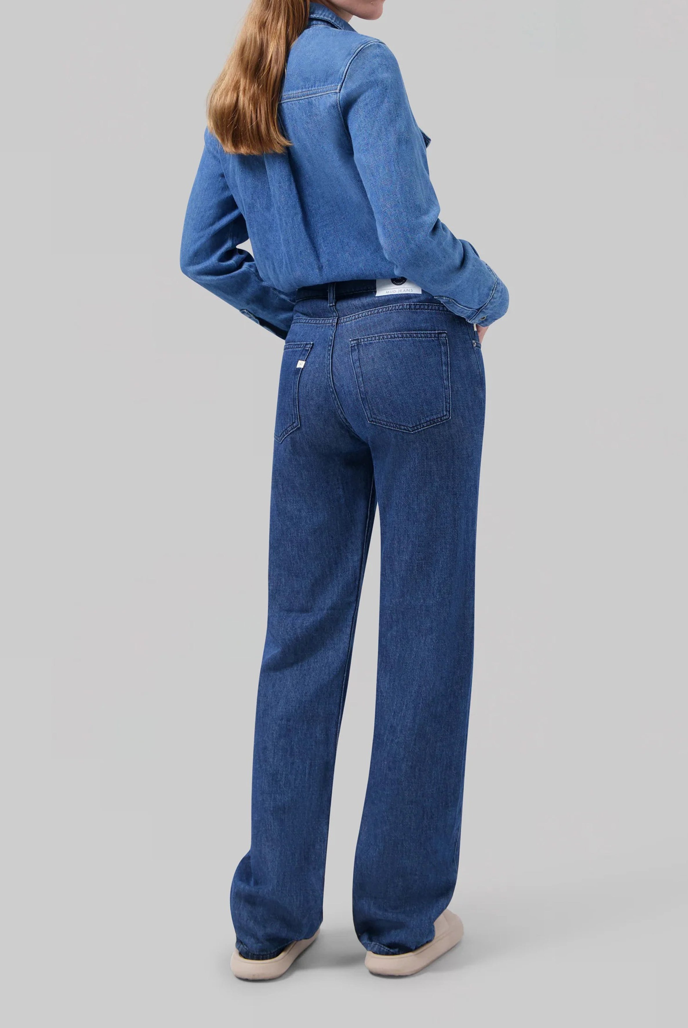 Woman in a blue denim jumpsuit with long sleeves, showcasing wide-leg pants, set against a neutral background.