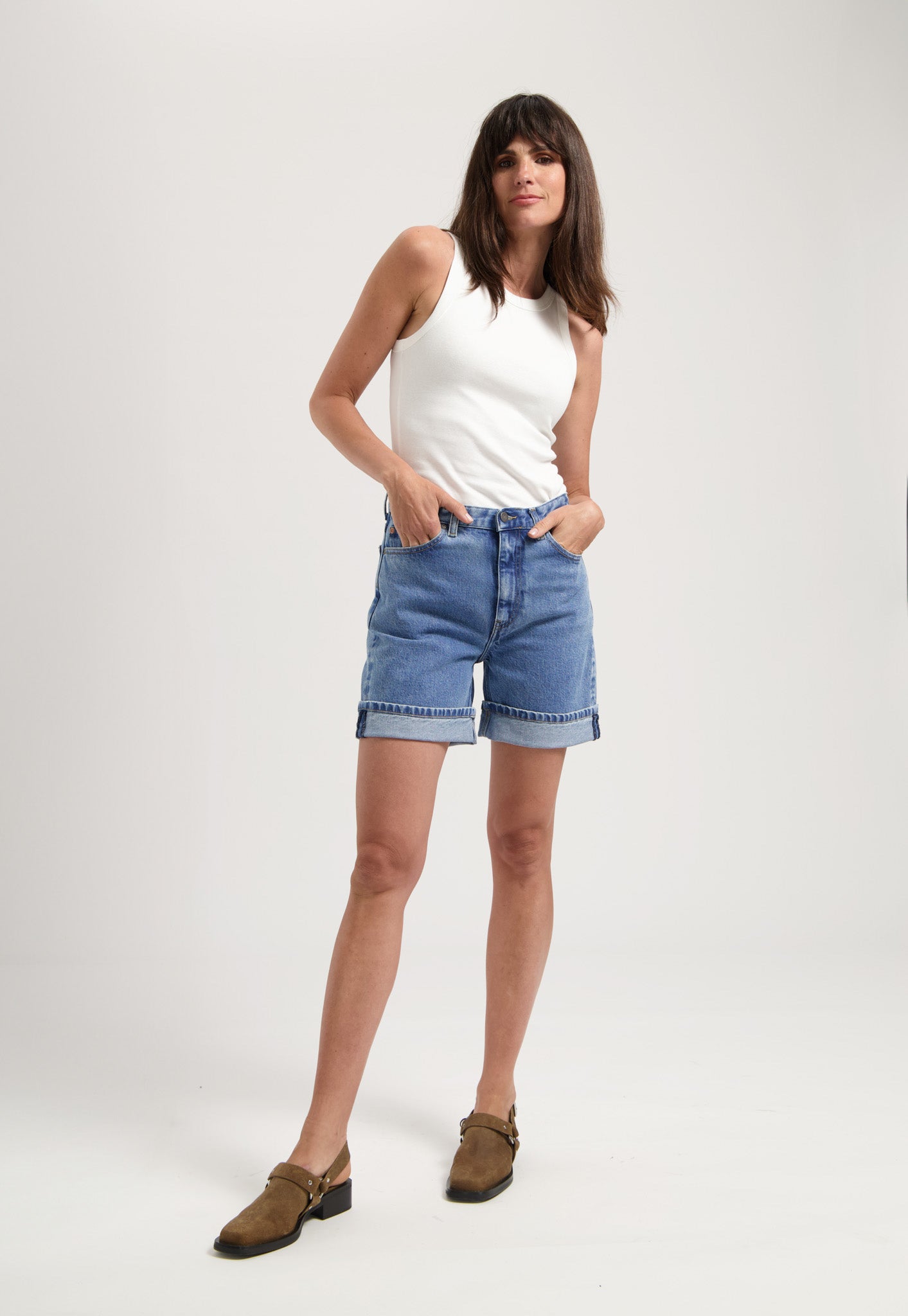 Casual summer outfit featuring a white sleeveless top paired with high-waisted light blue denim shorts and brown loafers.