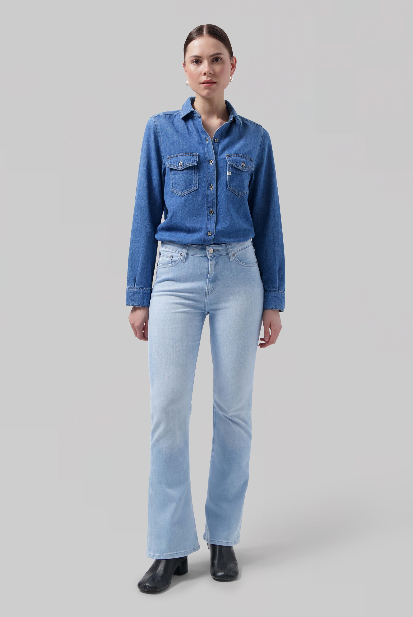 Model wearing a classic denim shirt with chest pockets and light blue bell-bottom jeans paired with black leather ankle boots.