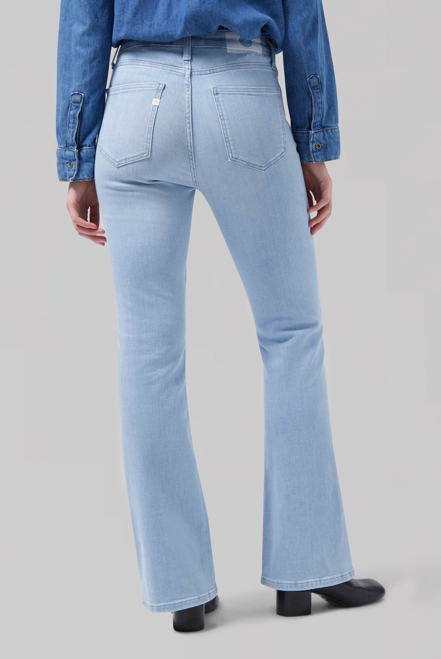 Light blue high-waisted denim jeans with a flared leg, paired with a denim shirt and black boots, showcasing a stylish back view.