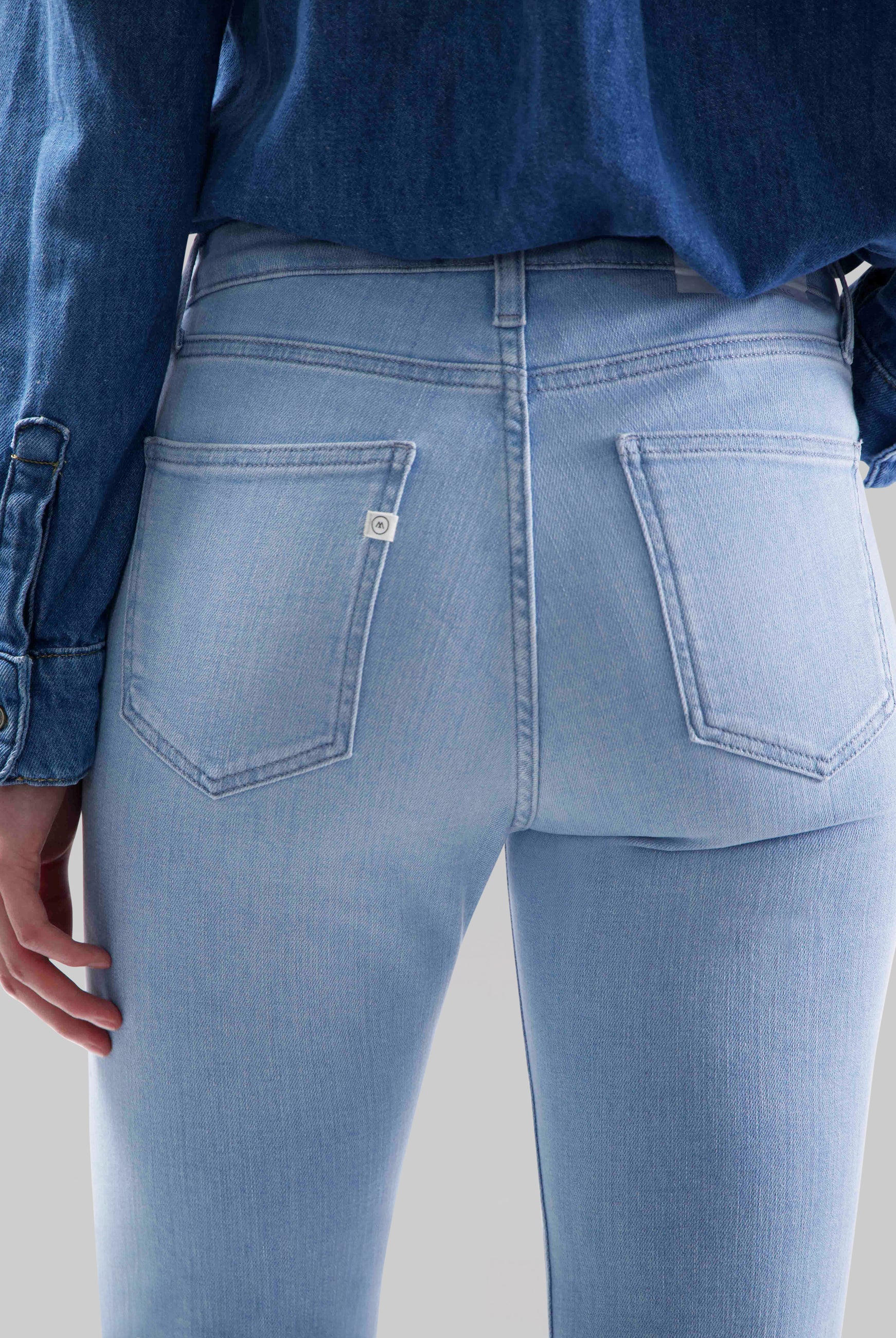 Light blue, high-waisted denim jeans with back pockets, paired with a dark blue denim shirt, showcasing a casual style.