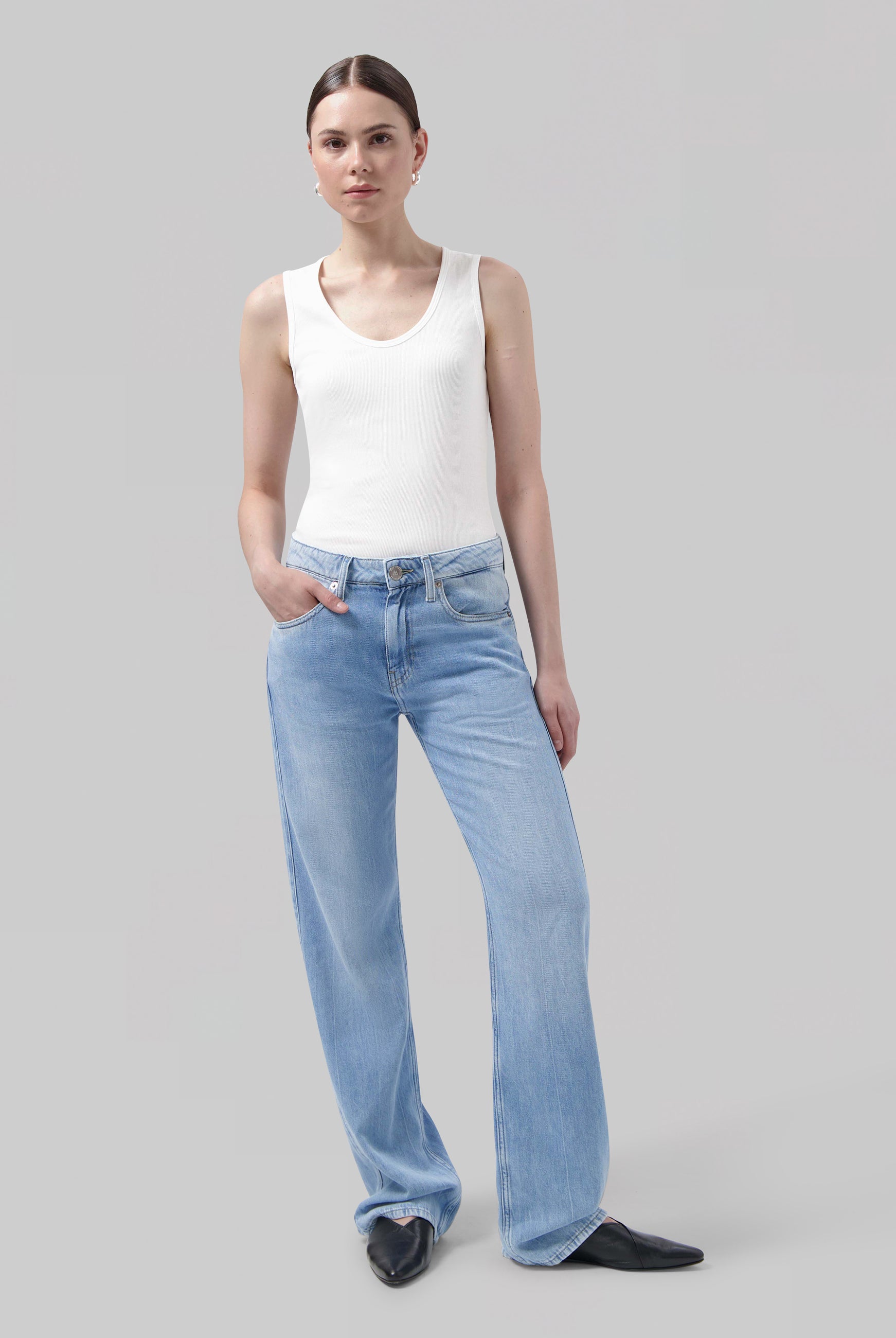 Woman wearing light blue wide-leg jeans with a fitted white tank top and black pointed shoes.