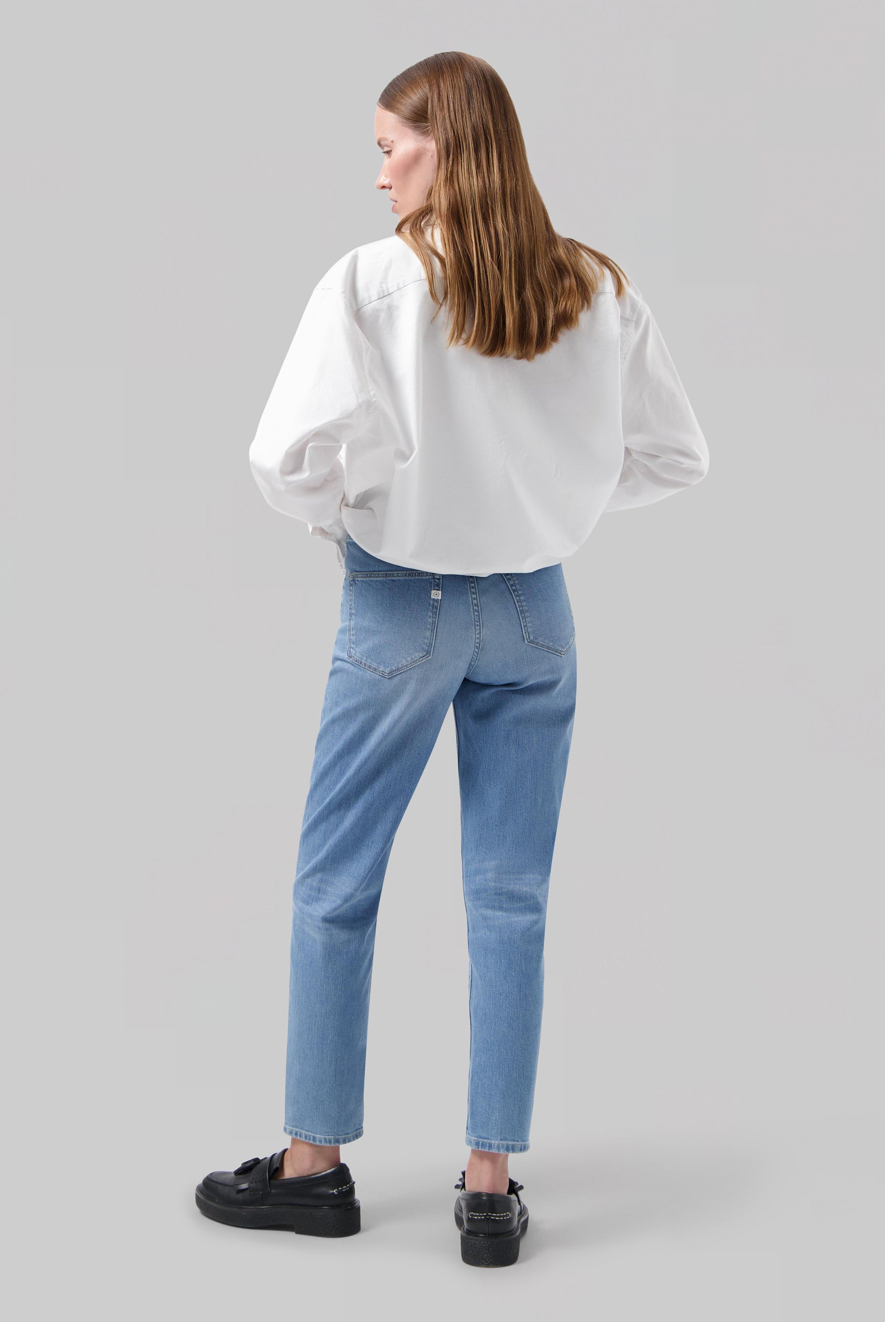 Woman wearing light blue straight-leg jeans with a relaxed fit, paired with a loose white shirt and black shoes.