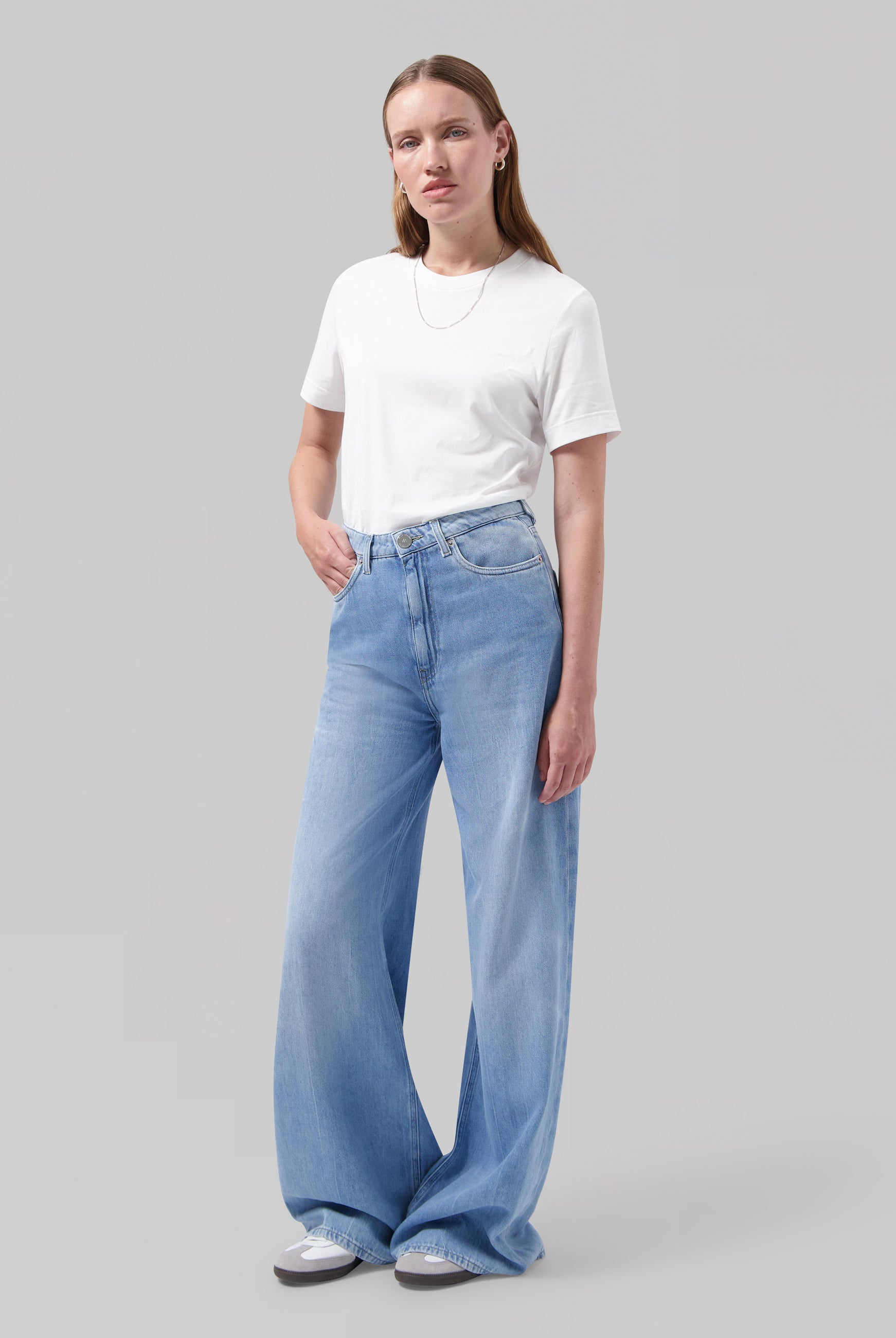 Woman in wide-leg, light blue denim jeans and plain white T-shirt, featuring casual style with relaxed fit jeans.
