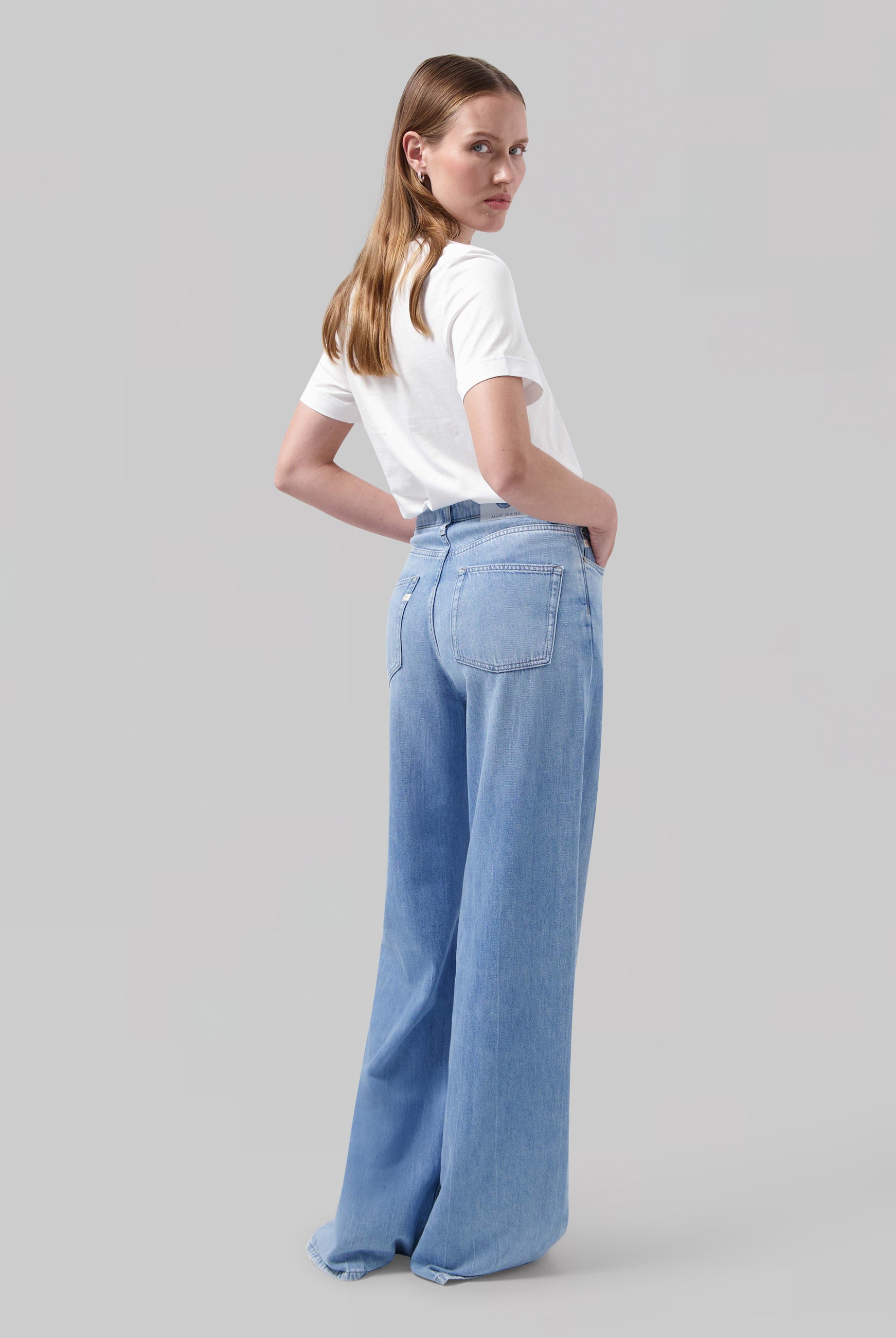 Woman wearing wide-leg light blue denim jeans with a high-waist fit shown with a simple white short-sleeve top.