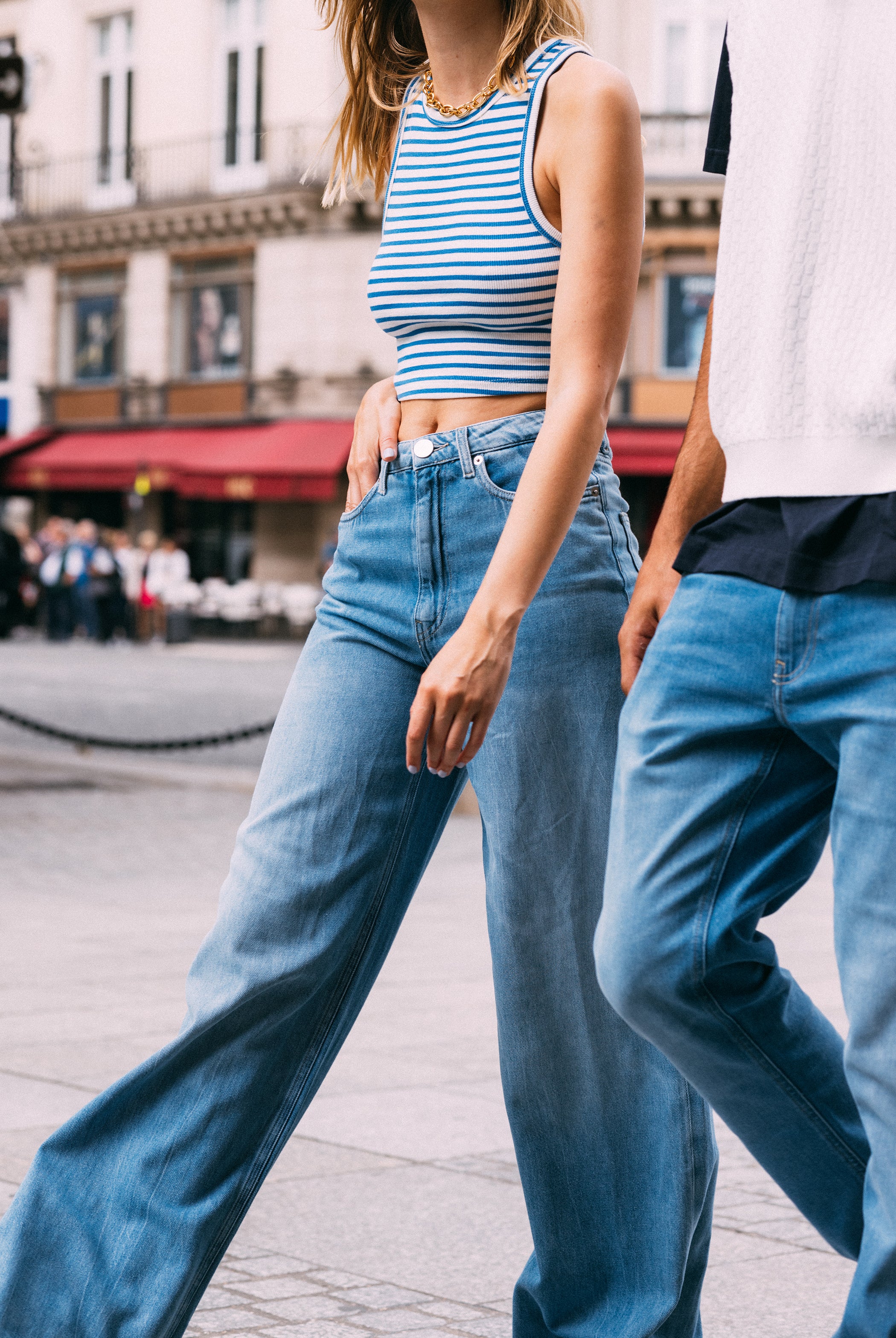 Casual streetwear featuring light blue high-waisted jeans paired with a blue and white striped sleeveless crop top.