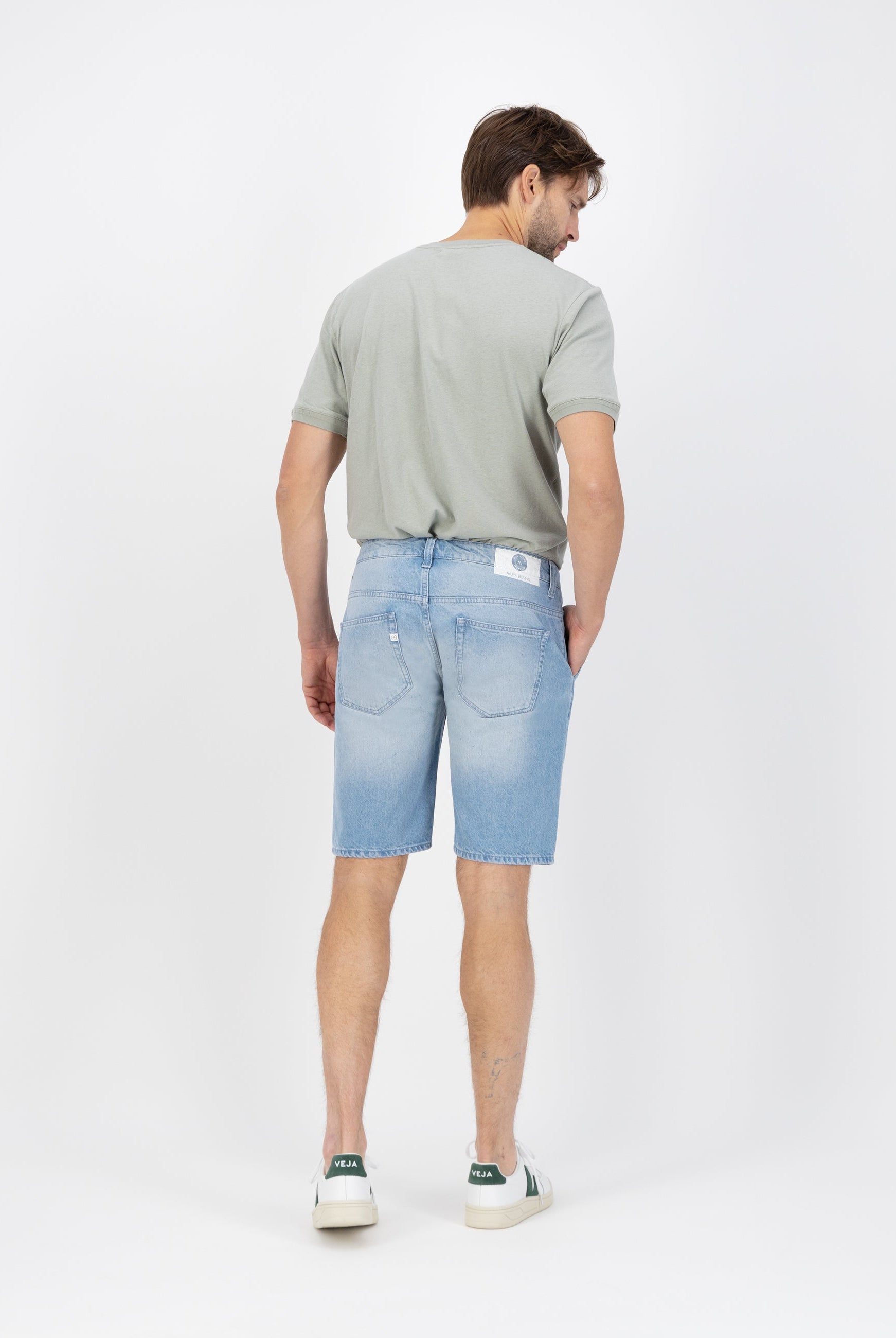 Sustainable MUD Jeans in light blue denim, crafted ethically from organic cotton, worn with casual white sneakers.