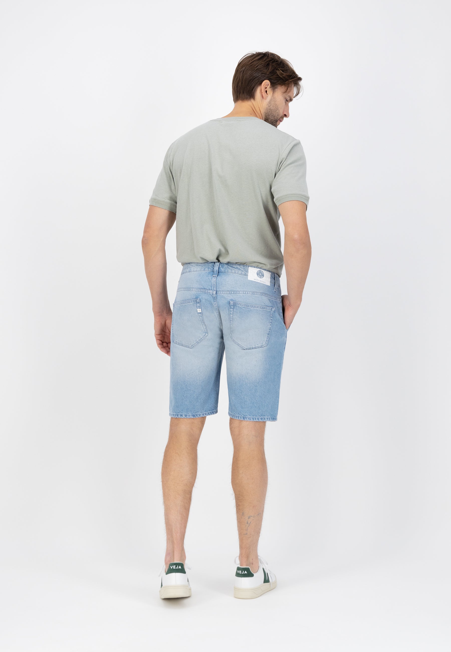 Sustainable MUD Jeans in light blue denim, crafted ethically from organic cotton, worn with casual white sneakers.