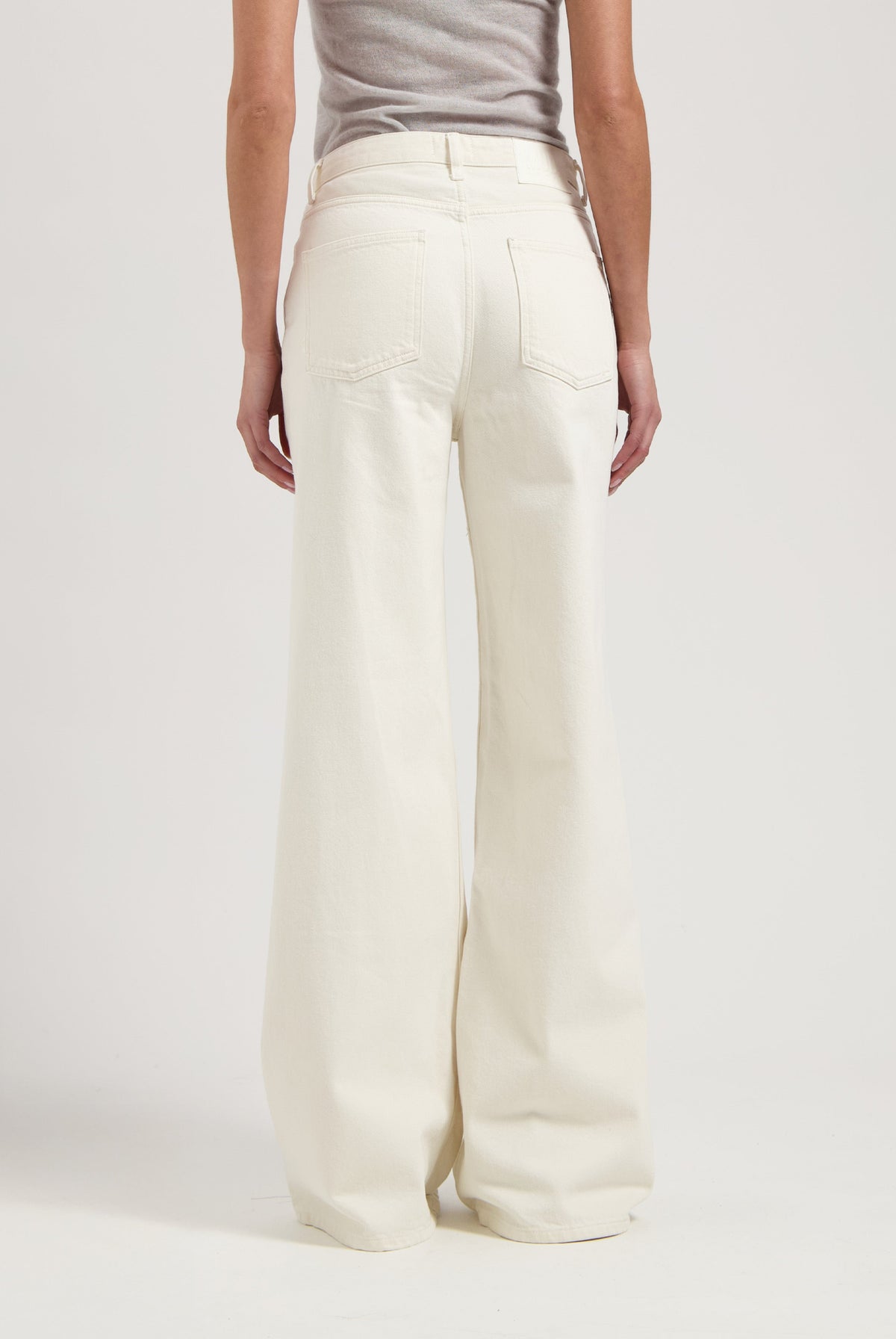 Wide-leg cream colored denim jeans showcased with a close-up back view, paired with a simple gray top.