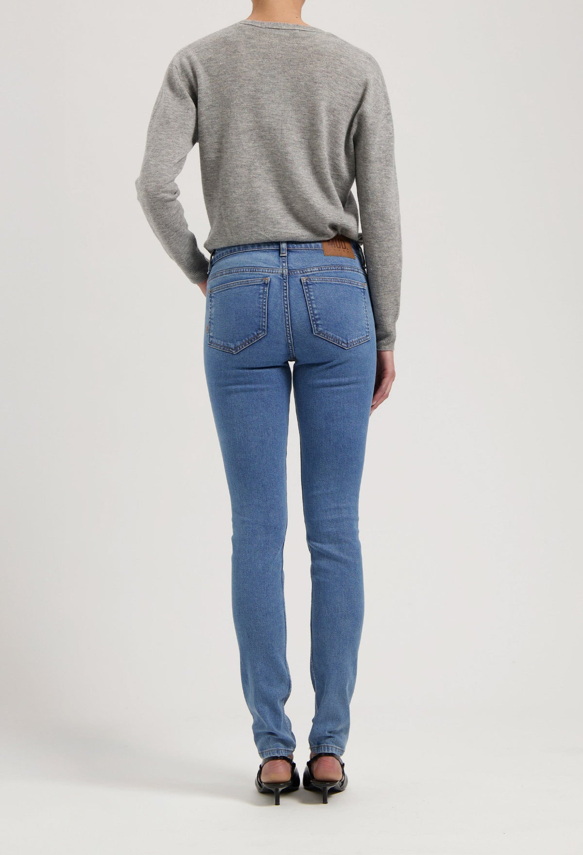 Rear view of a person in blue slim-fit jeans and a gray long-sleeve sweater, standing on a neutral background.