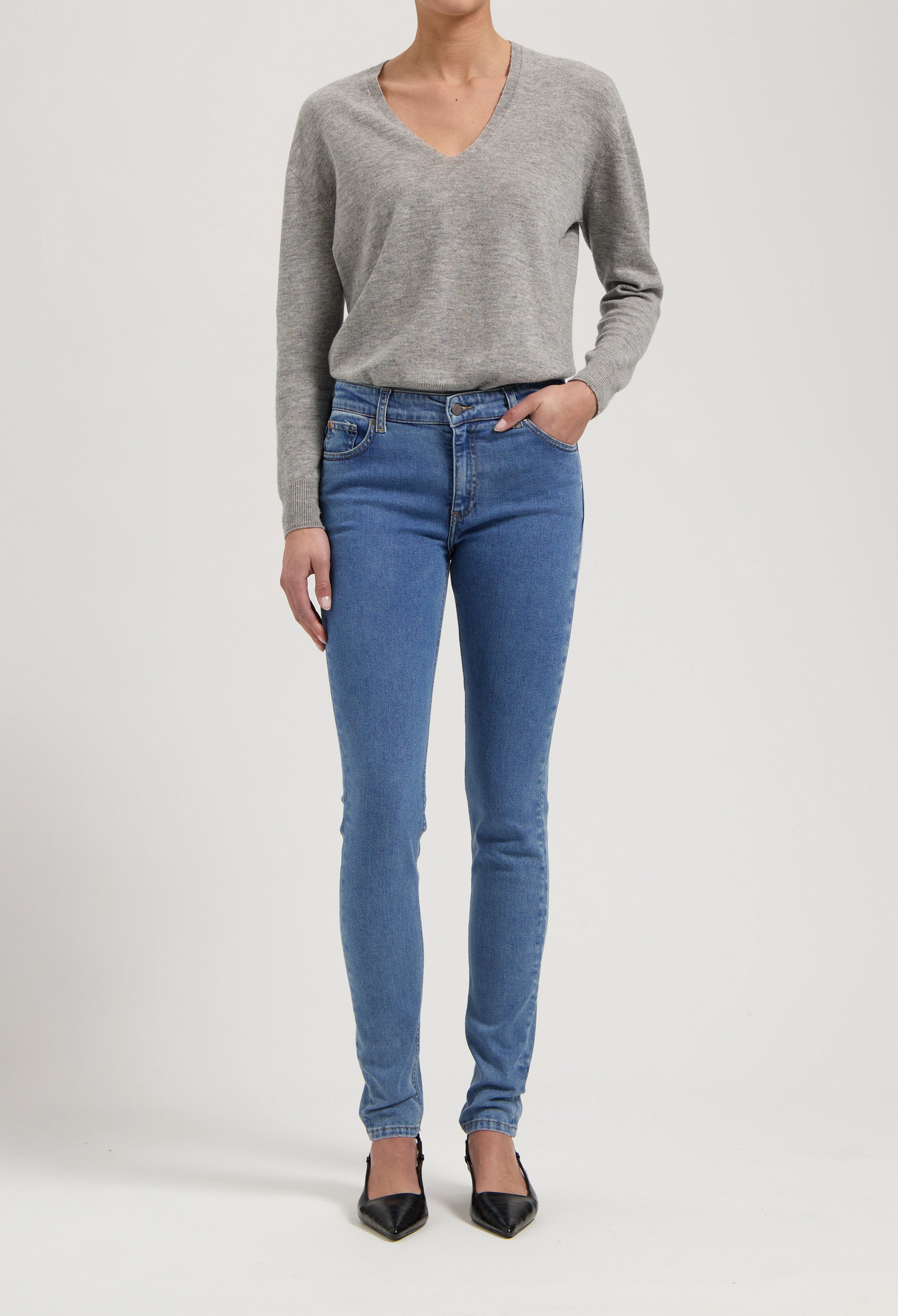 Gray long-sleeve V-neck top paired with fitted blue jeans and black pointed heels, showcasing casual yet stylish attire.