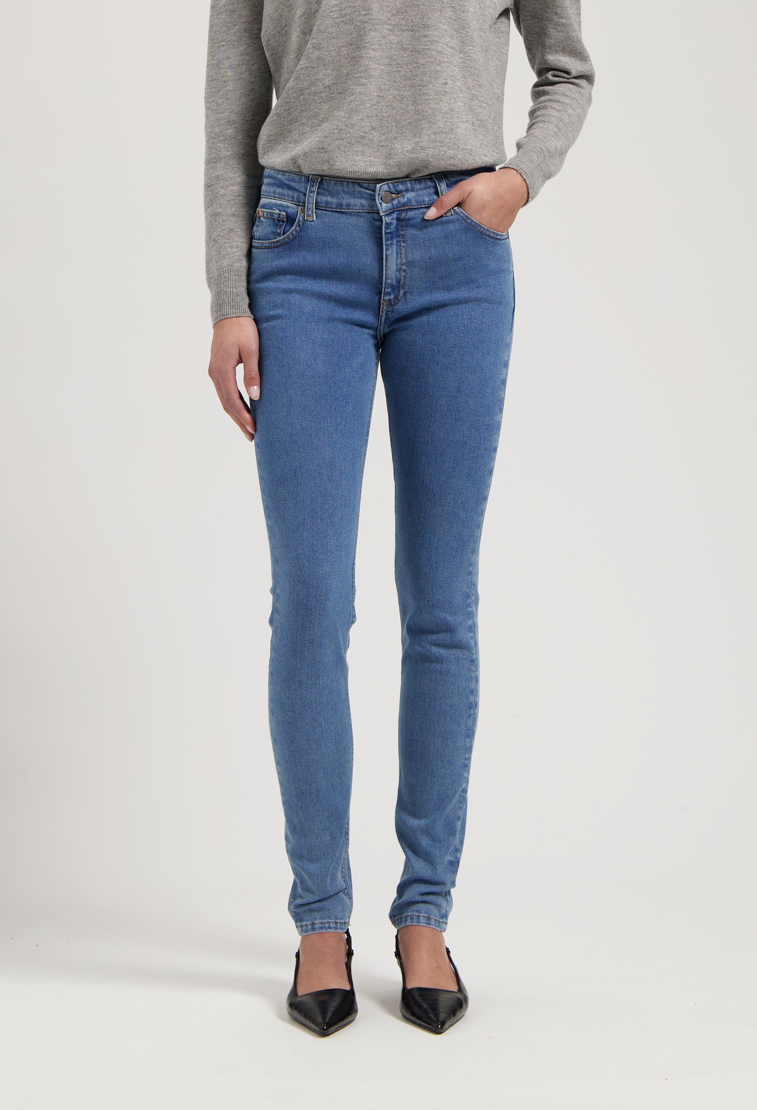 Casual blue slim-fit jeans made from organic cotton, worn with a gray sweater, showcasing a stylish and comfortable look.