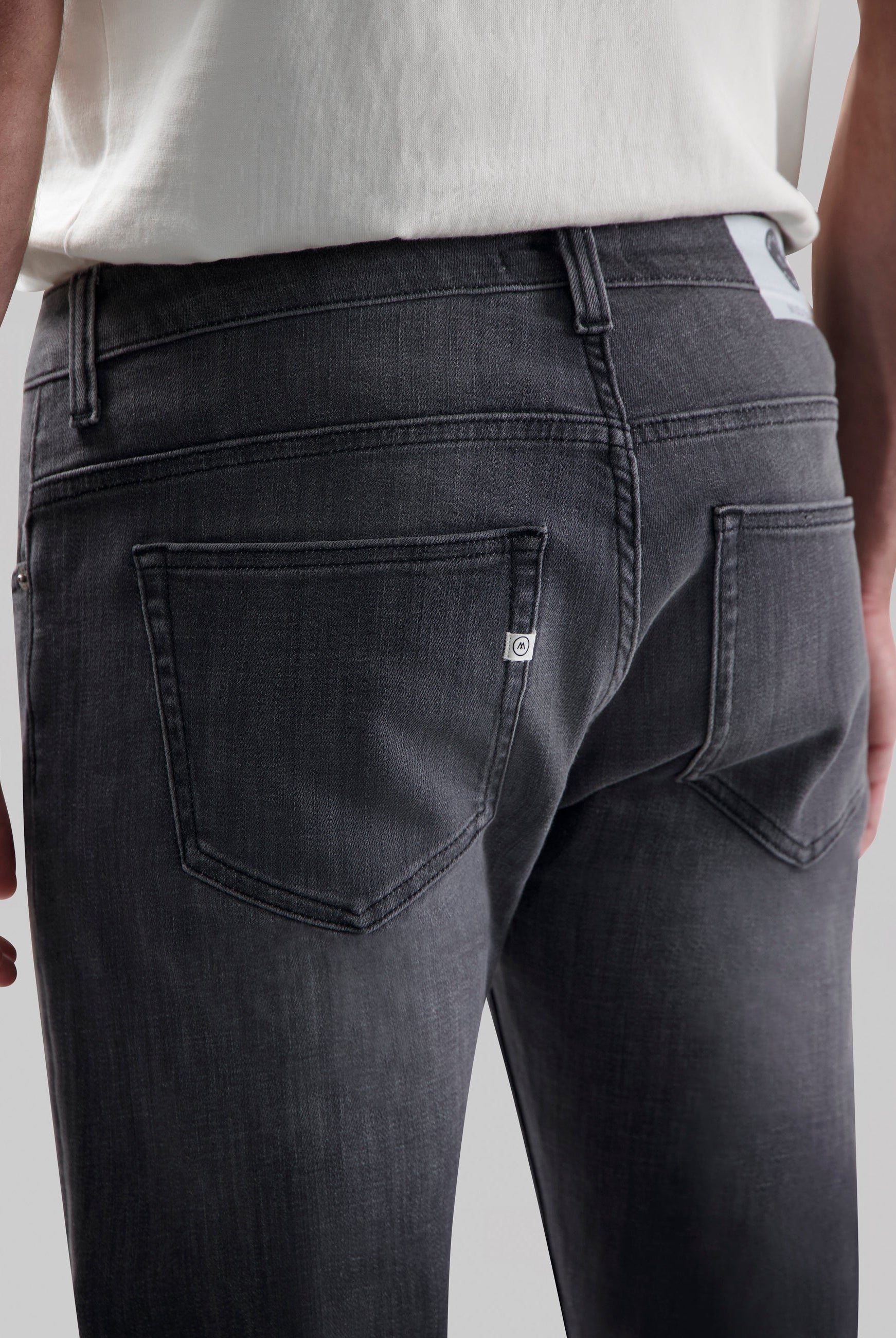 Sustainable MUD Jeans in light blue denim, crafted ethically from organic cotton, shown from the back with a white tee.