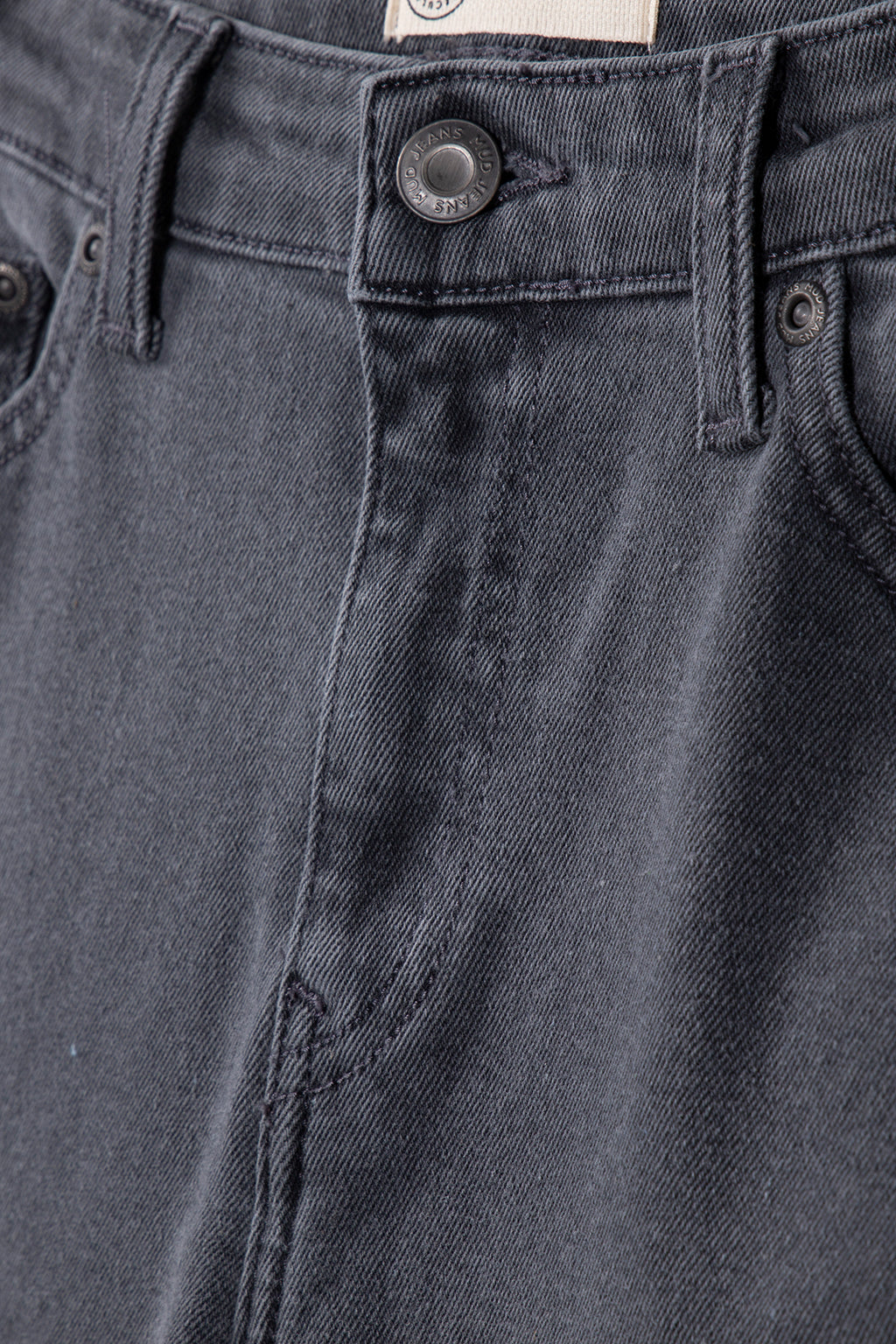Close-up of sustainable dark gray denim jeans showcasing detailed stitching and a branded button on the waistband.