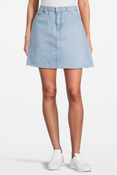 Light blue A-line denim skirt with front button and pocket details, paired with casual white sneakers, on a white background.