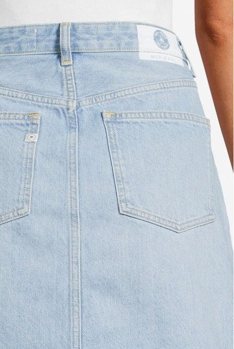 Light blue denim skirt made from organic cotton, featuring rear pockets and visible stitching, worn with a white top.