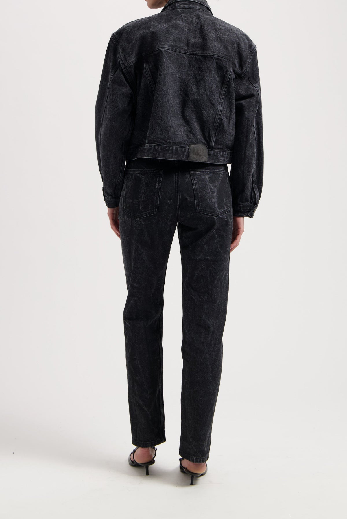 Black denim jacket and jeans set from MUD Jeans, featuring a textured finish, worn with strappy black sandals.